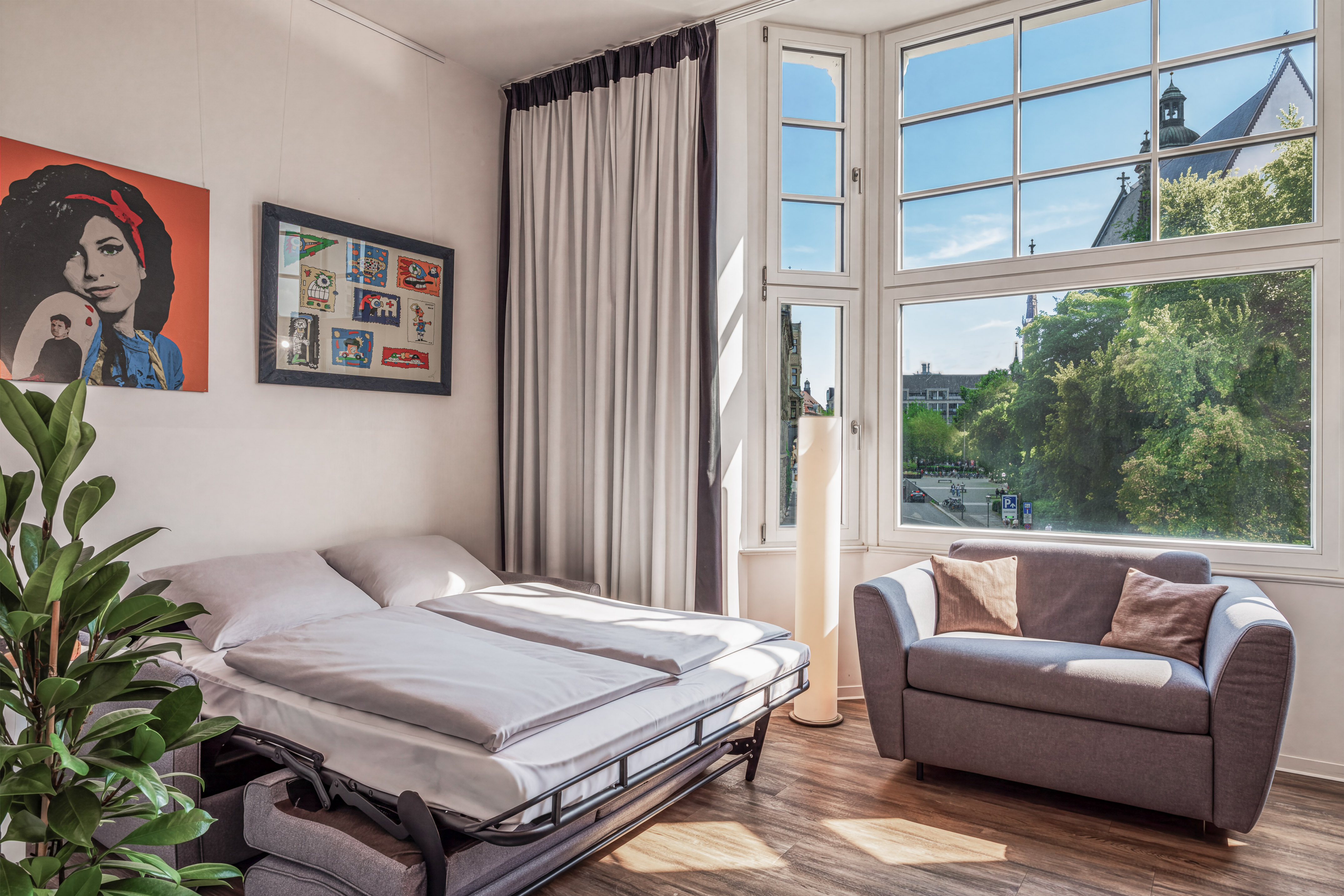 Modern studio with sofa bed, gray couch, and city view window.