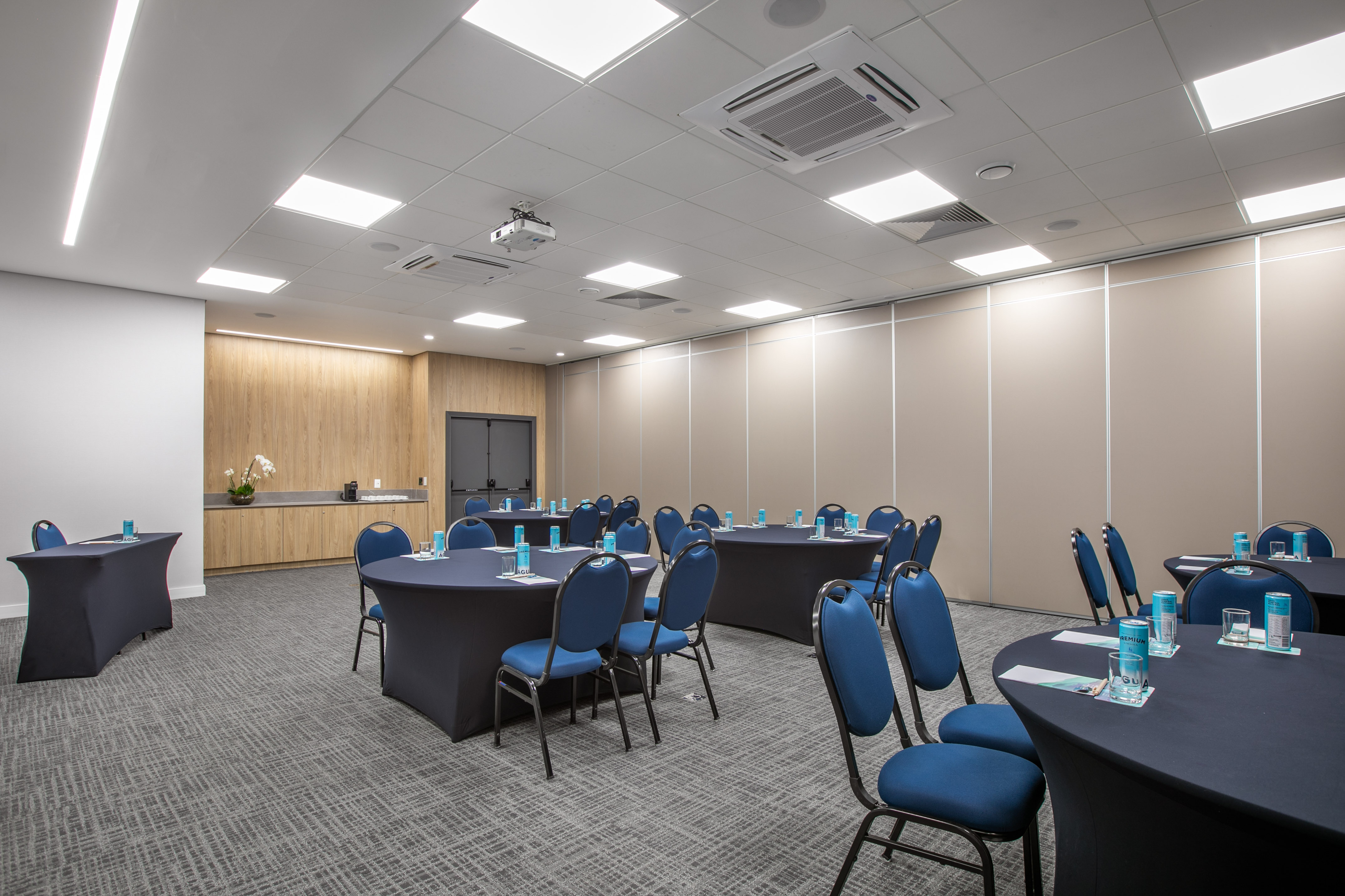 Modern conference room with black round tables, blue chairs, and projector.