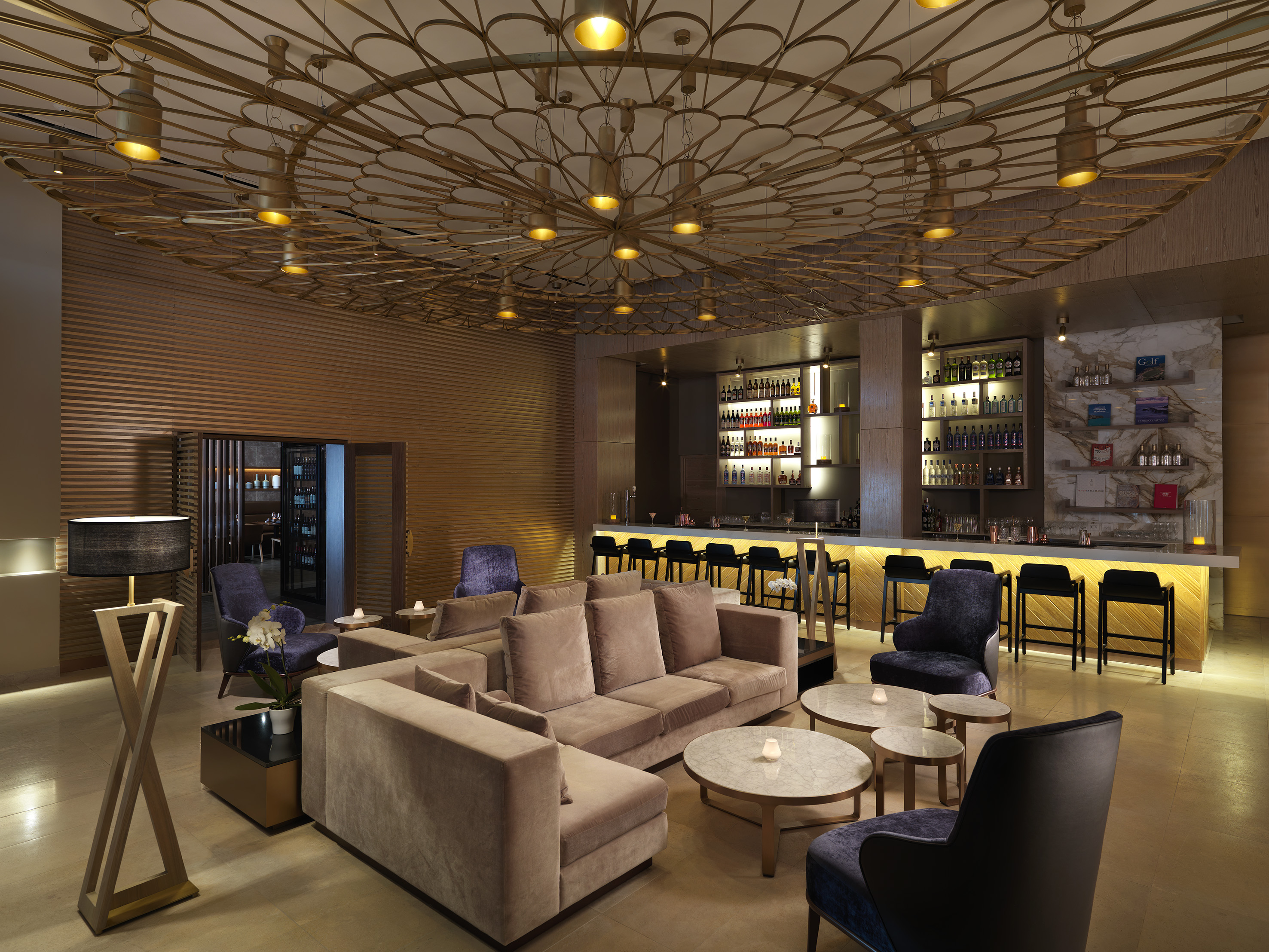 Luxury hotel lounge bar with ornate gold ceiling, plush seating, and illuminated bar.