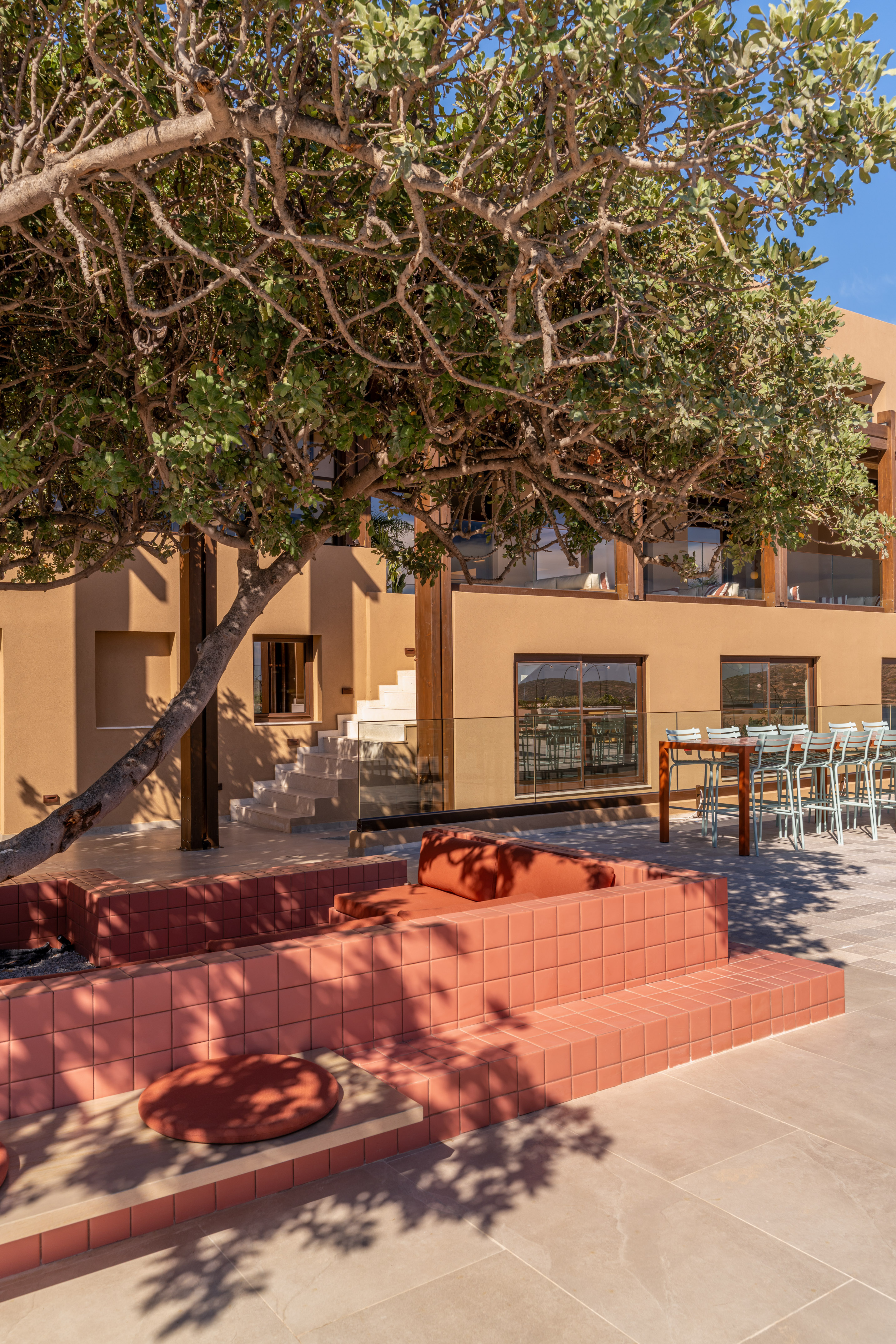 Outdoor lounge of a modern resort with terracotta seating and lush tree.