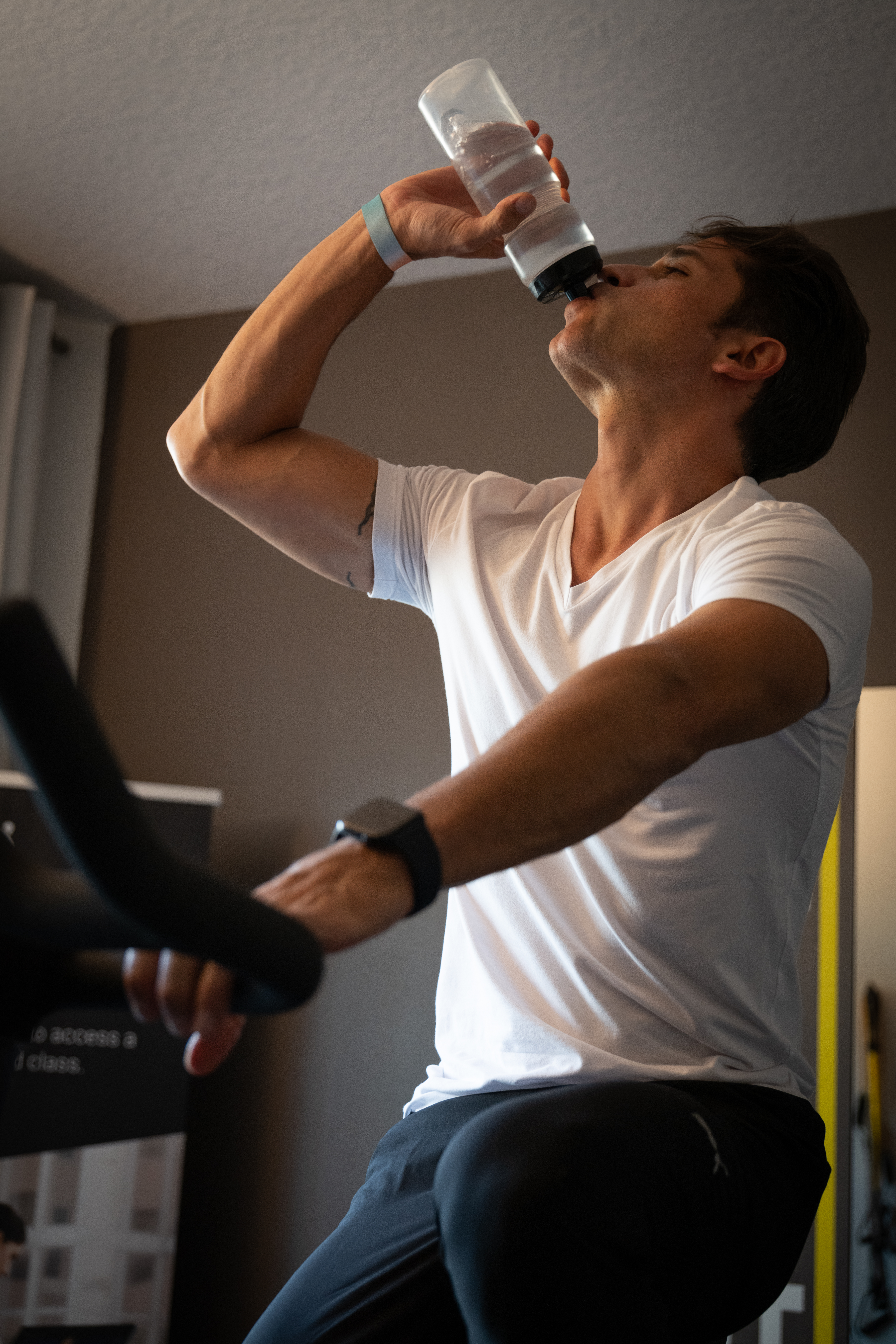 Man hydrating with water bottle during home bike workout.