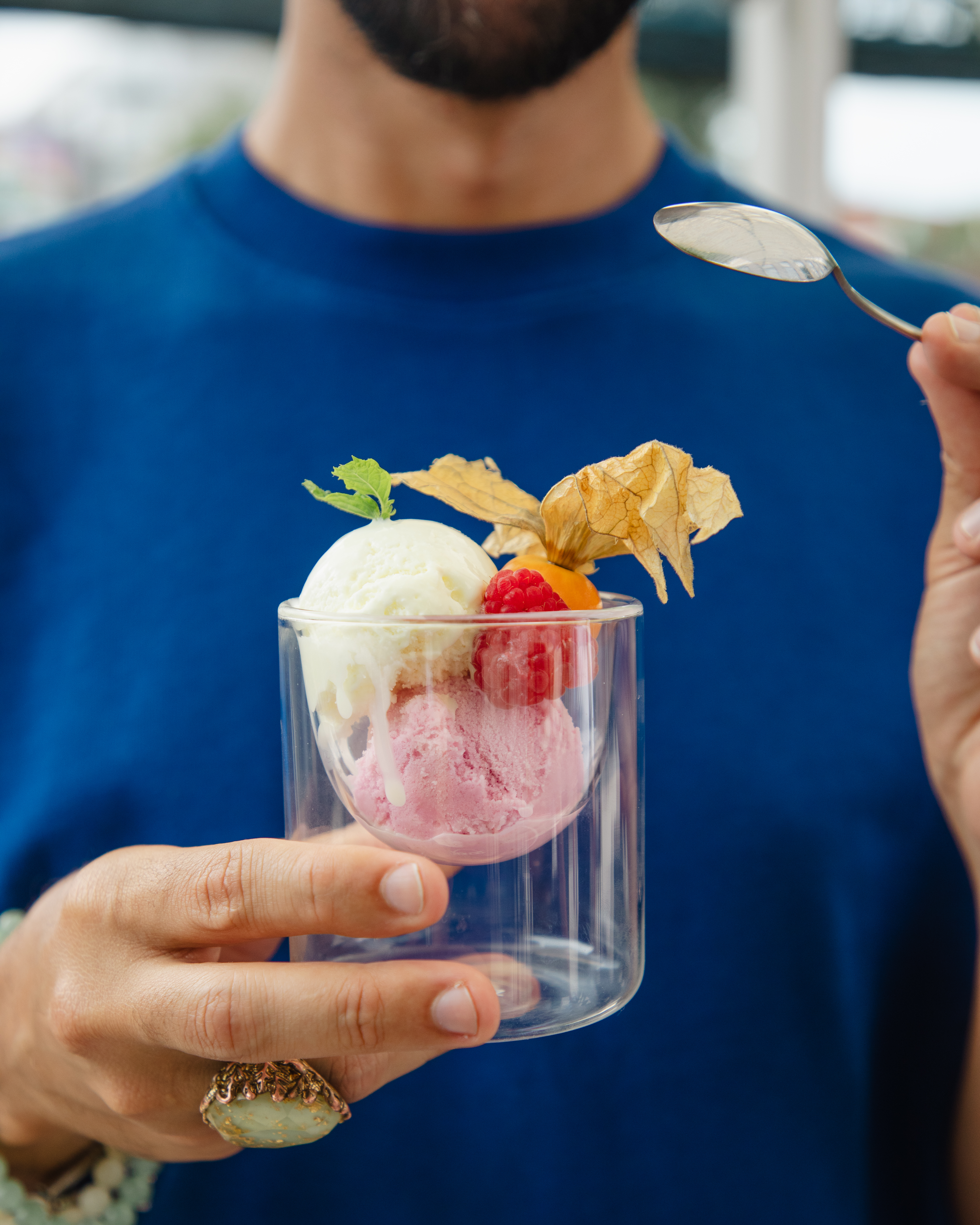 Man holding scoops of vanilla and raspberry ice cream with berries and mint.