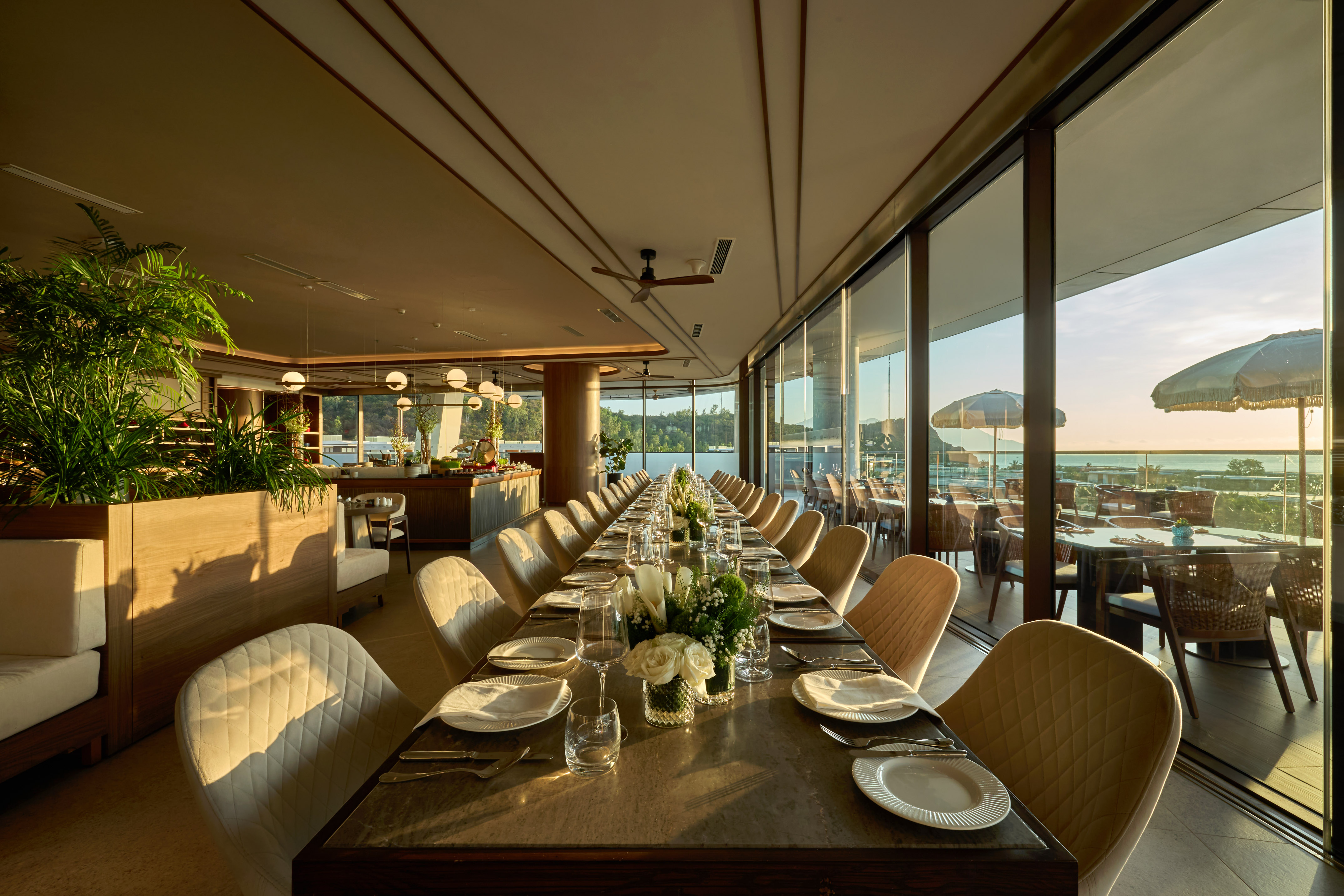 Elegant long dining table, ocean view luxury restaurant at sunset.