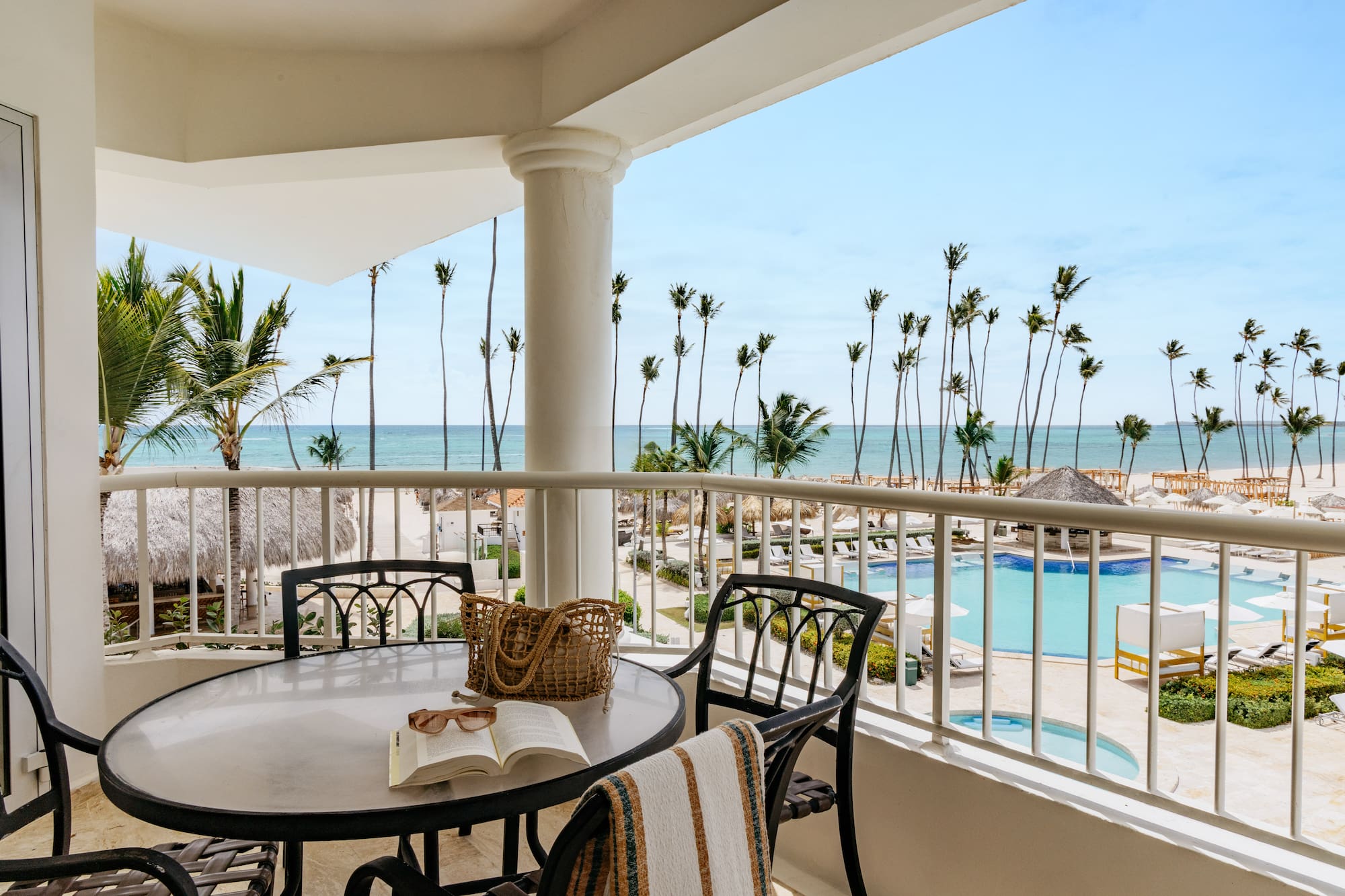 Oceanfront balcony overlooking tropical beach, palm trees, and resort pool.