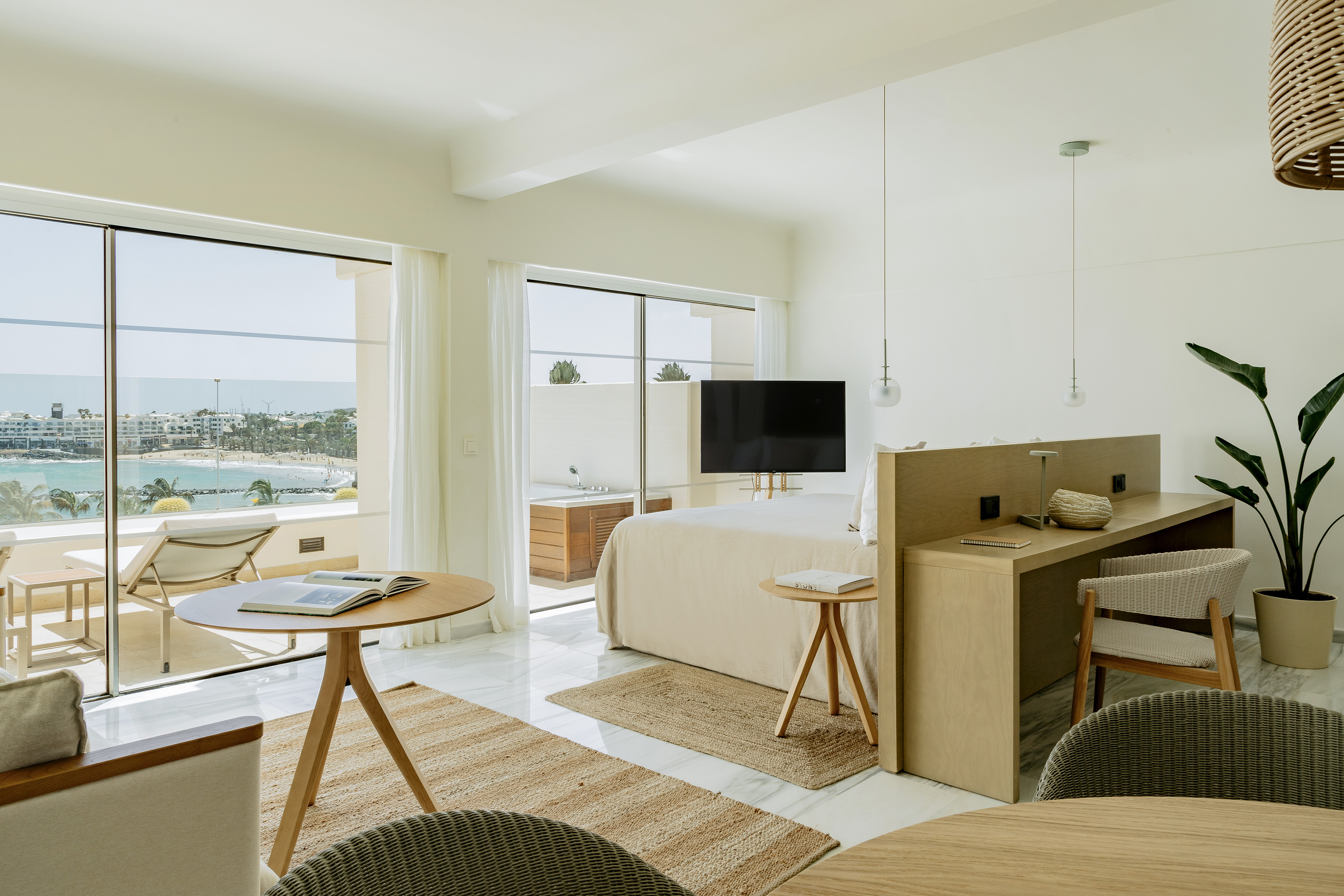 Modern hotel suite with ocean view, balcony, large bed, and natural decor.