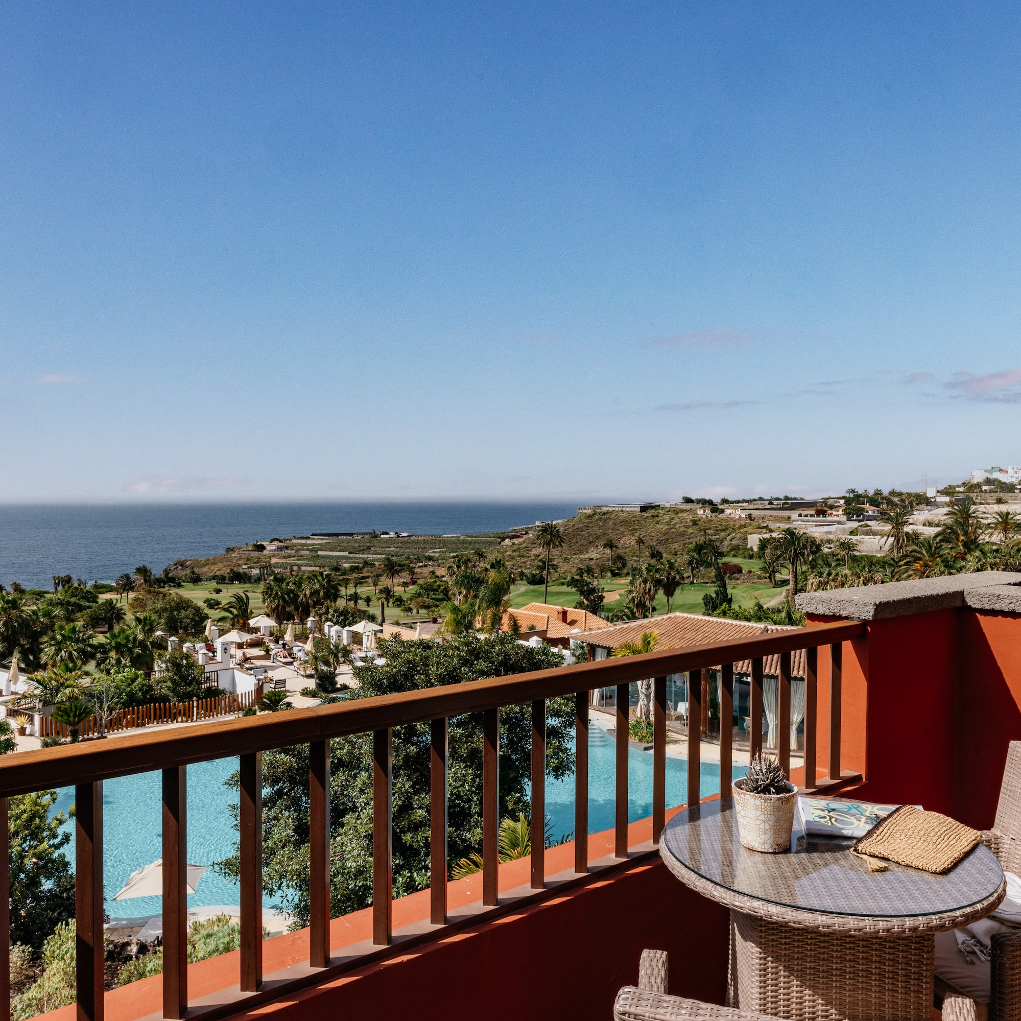 Tropical resort balcony overlooking ocean, pool, and palm trees.
