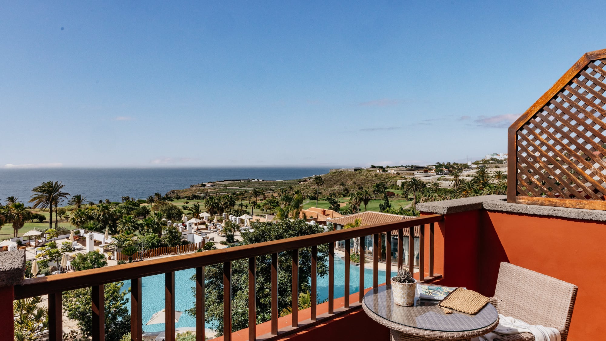 Tropical resort balcony overlooking ocean, pool, and palm trees.