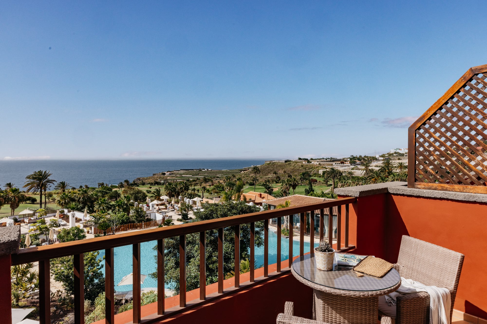 Tropical resort balcony overlooking ocean, pool, and palm trees.