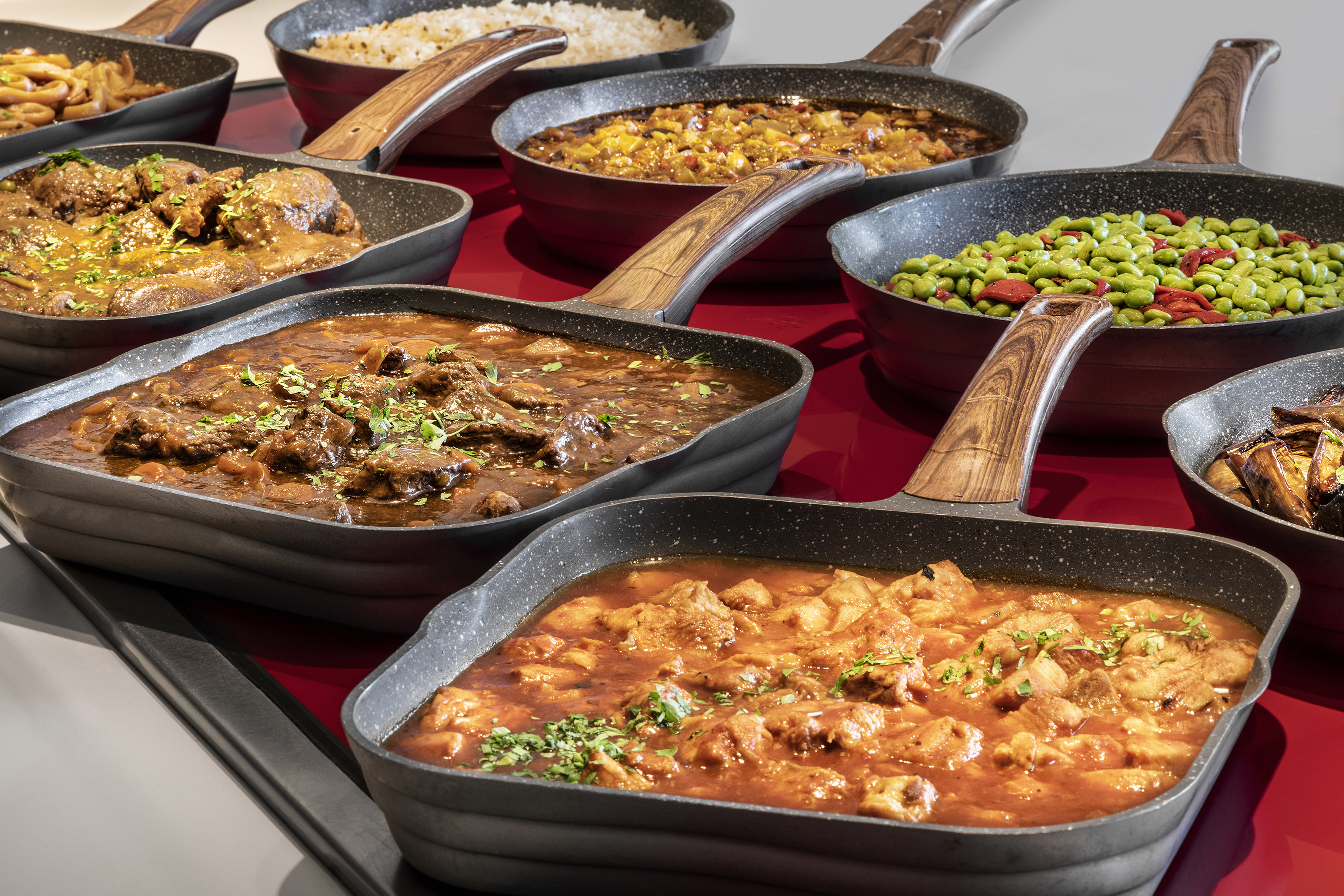 Hot buffet dishes: stews, rice, and vegetables in square non-stick pans.