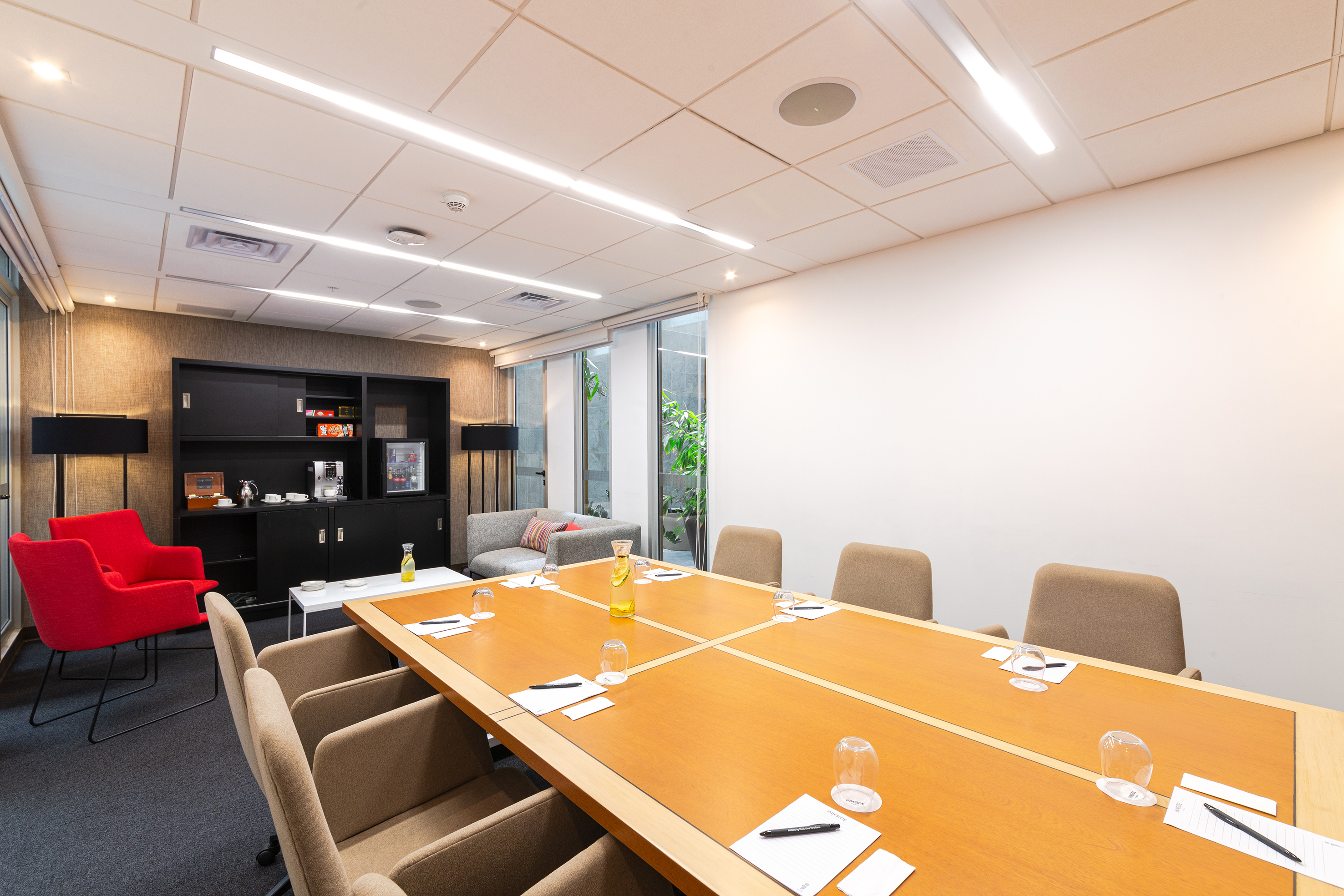 Modern boardroom with long table, office chairs, and refreshment station.