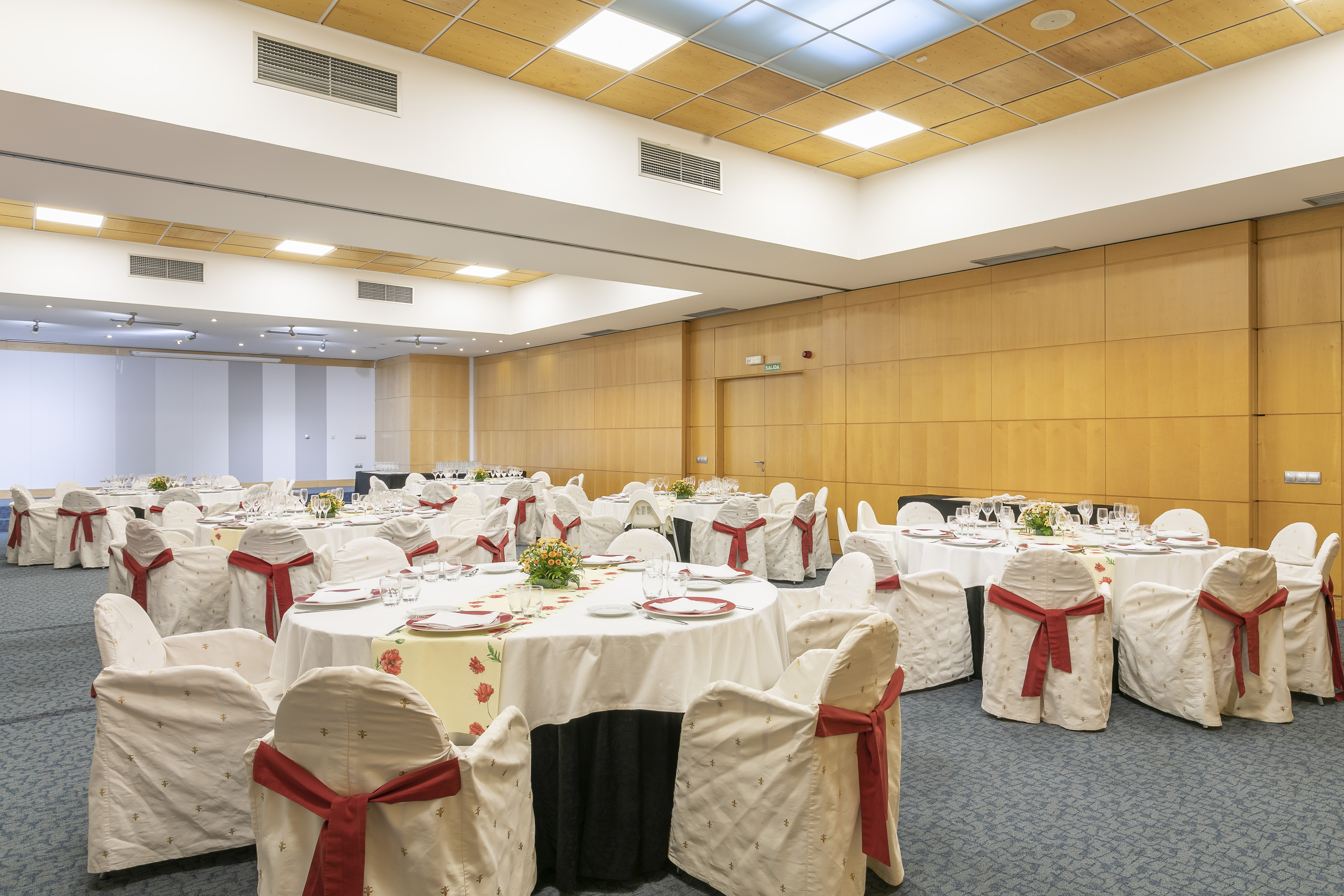 Elegant event space with round dining tables, white chair covers, and red sashes.