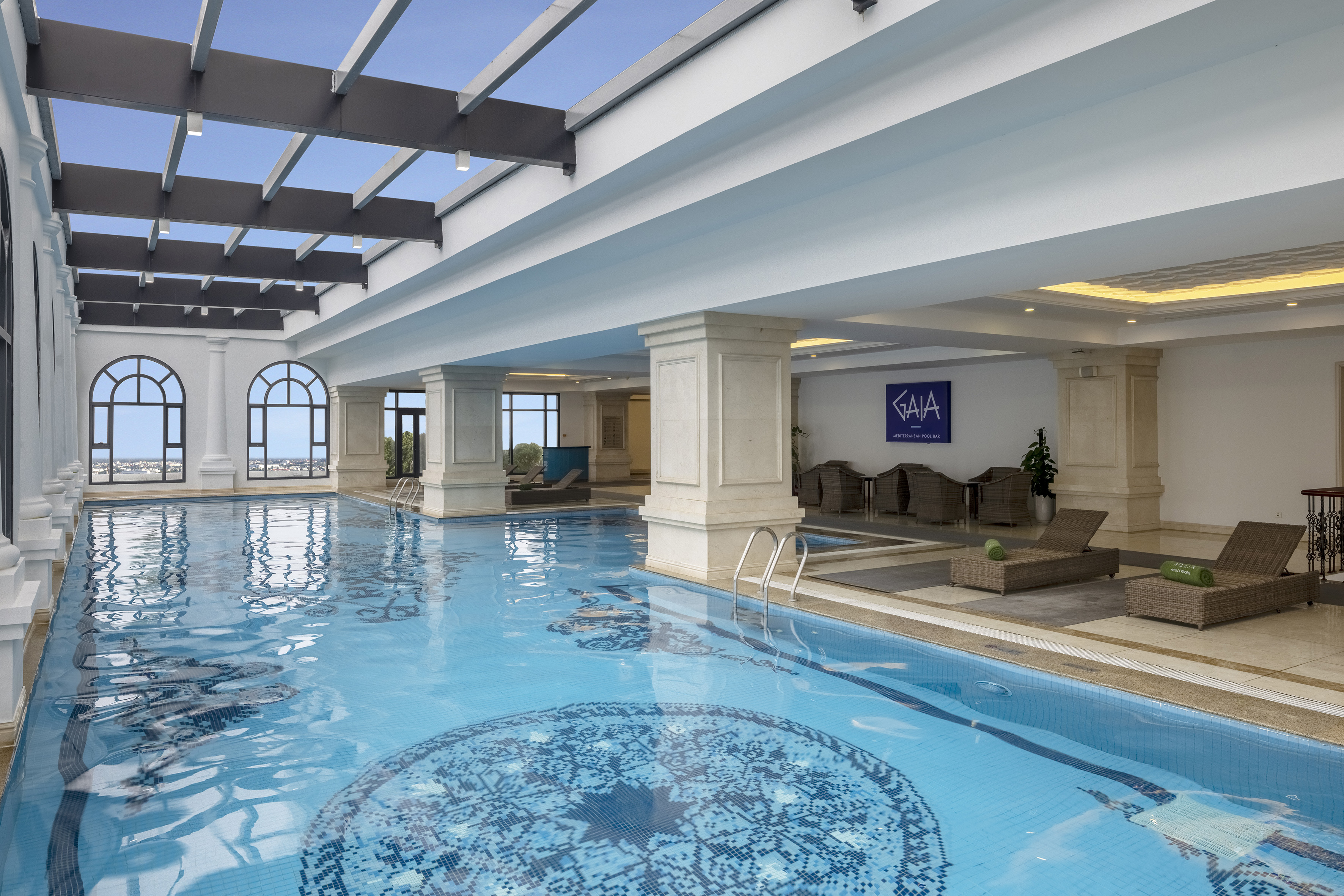 Luxury indoor hotel pool with blue mosaic tiles, arched windows, and lounge chairs.
