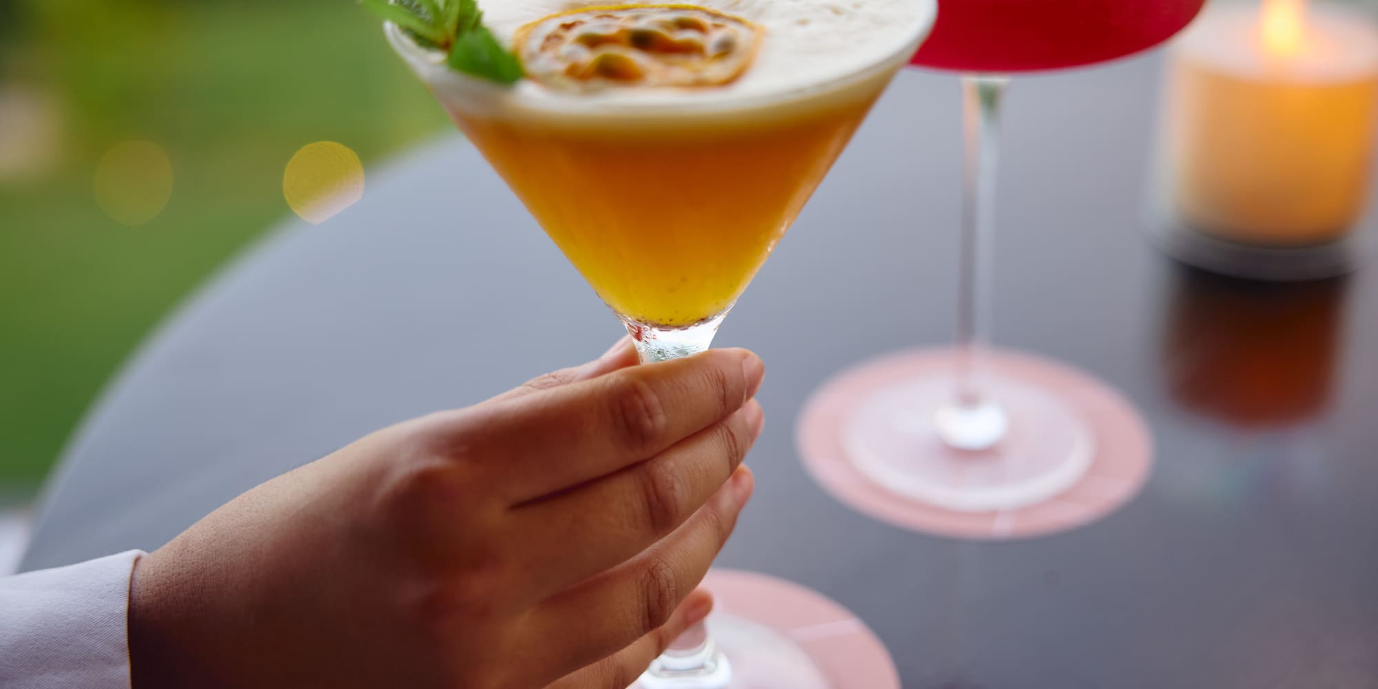 Hand holds passion fruit martini with mint. Red cocktail, candle.