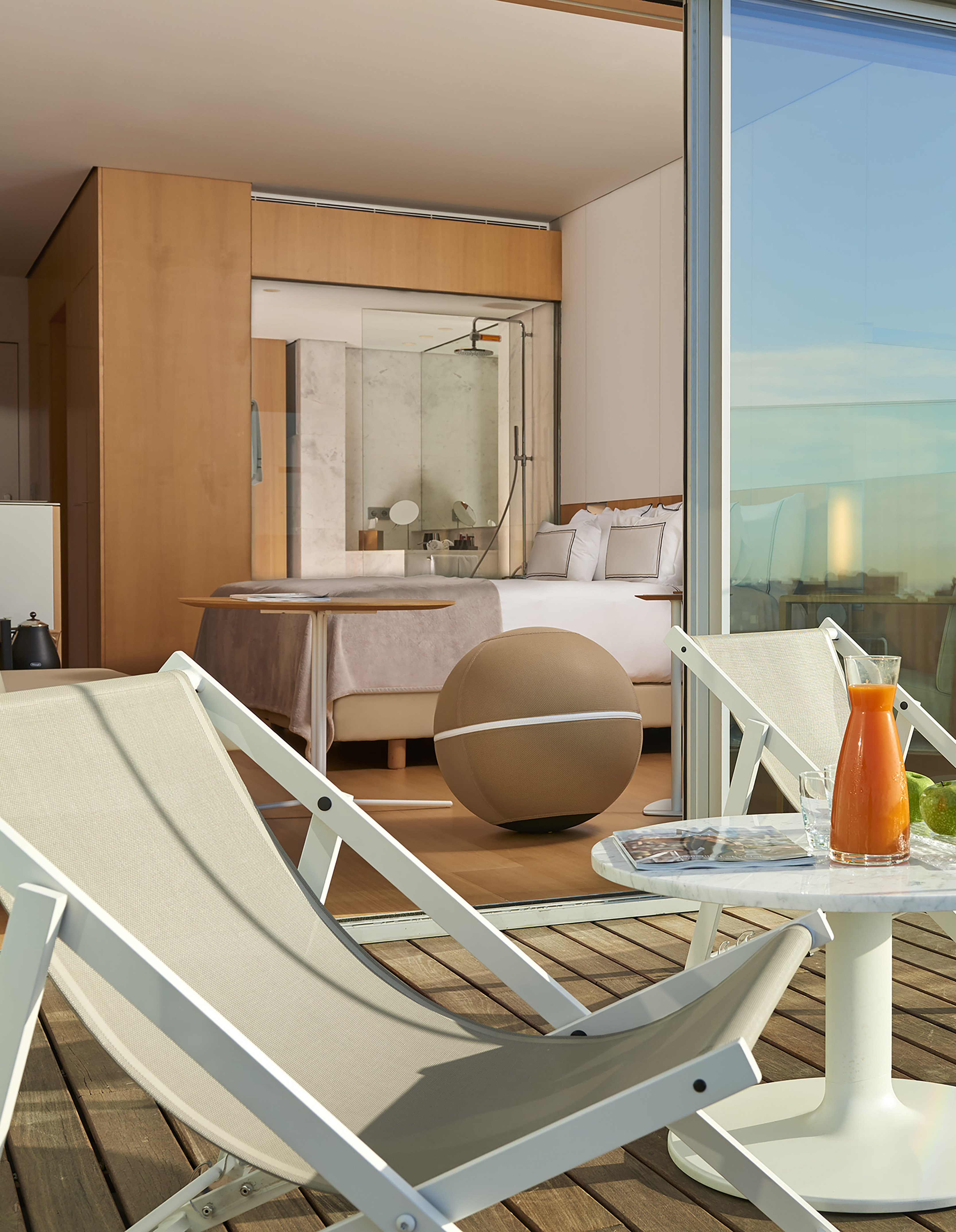 Luxury hotel suite balcony with deck chairs, marble table, and orange juice.