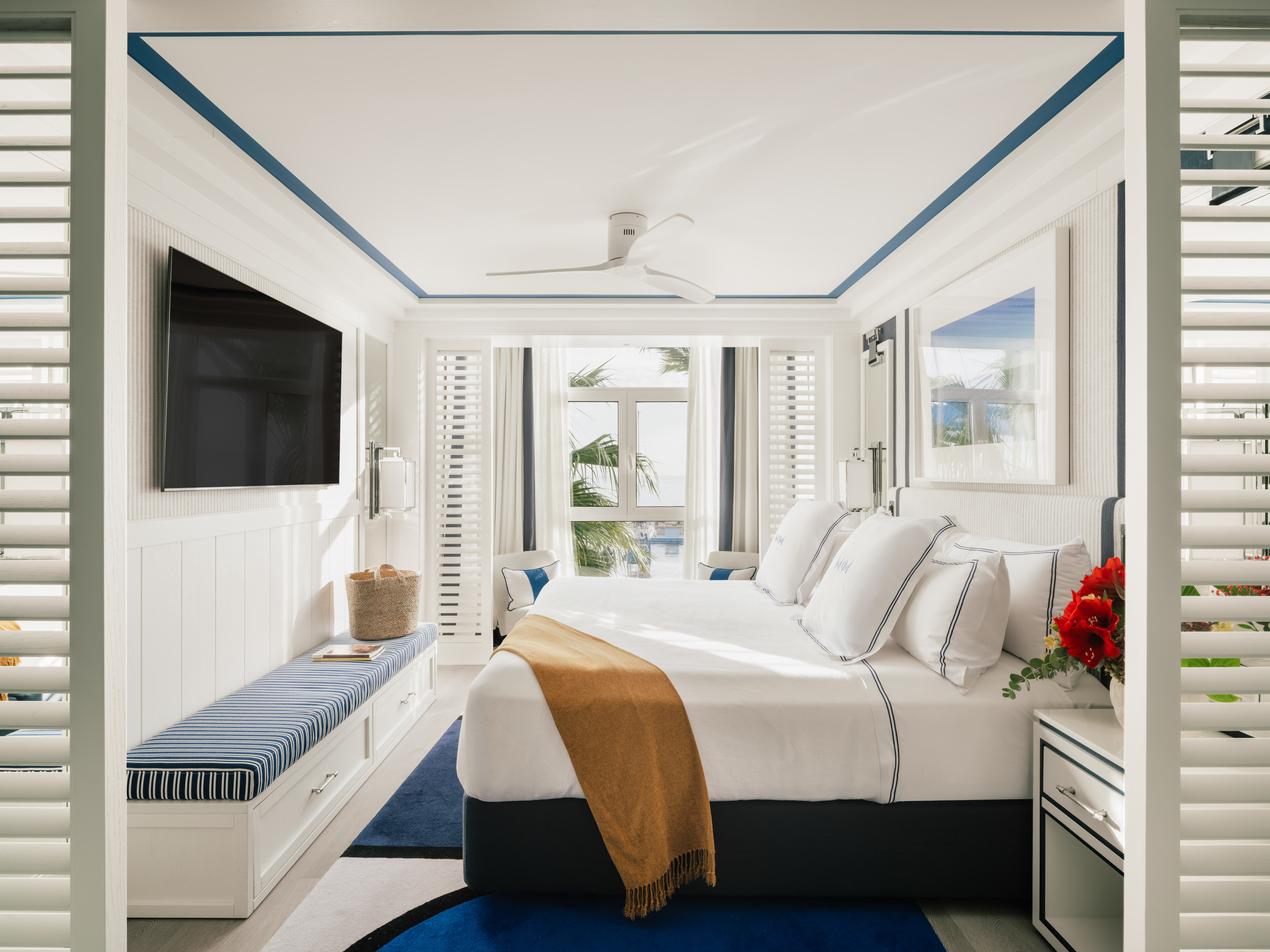 Luxury hotel bedroom in white and blue, featuring a large bed and tropical view.