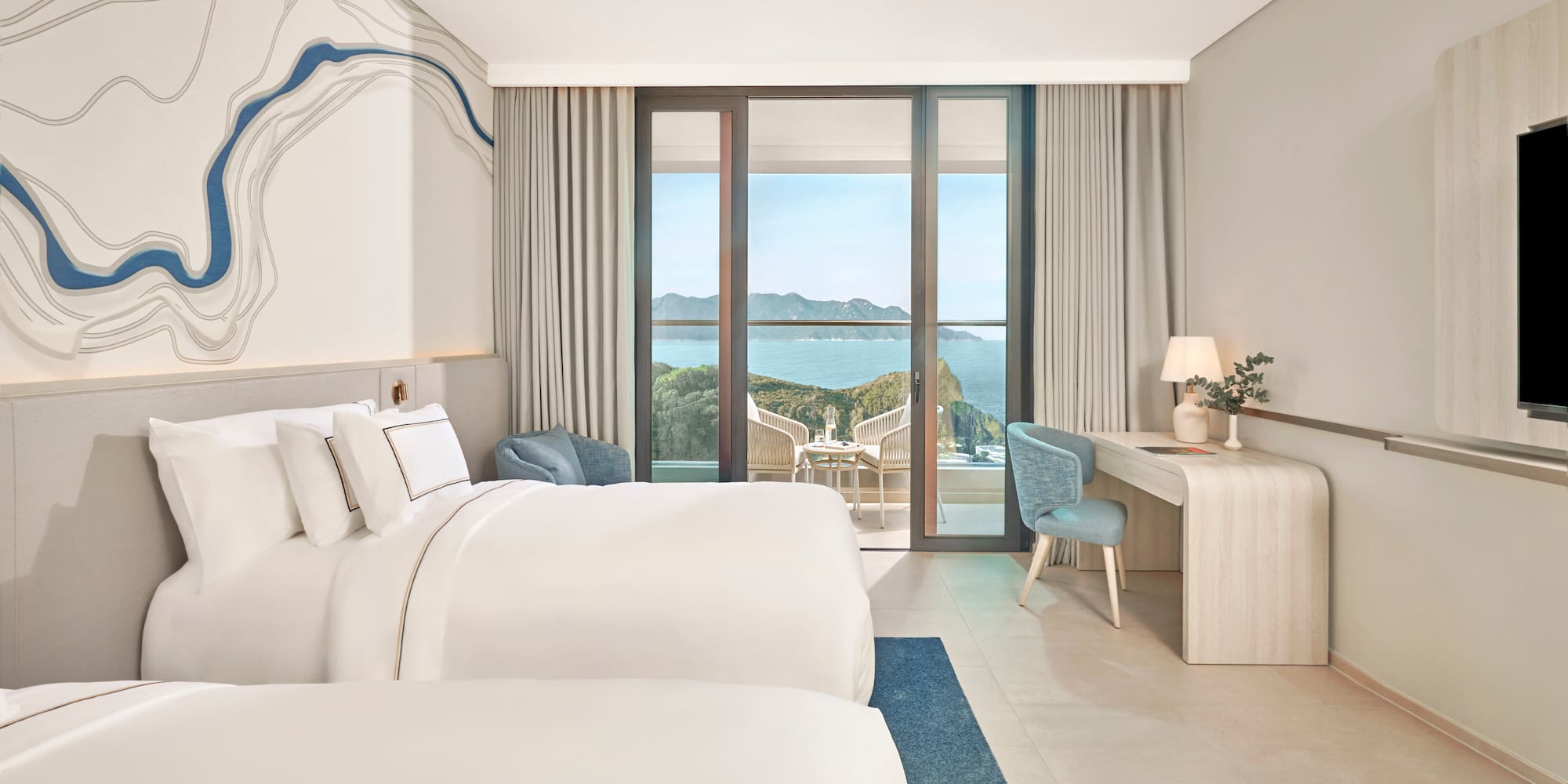 Bright hotel room with two beds, large balcony overlooking ocean and cliffs.