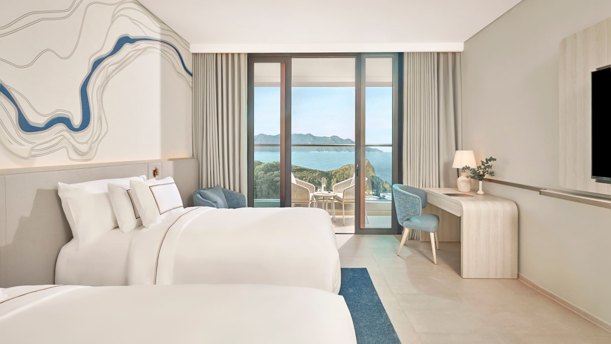 Bright hotel room with two beds, large balcony overlooking ocean and cliffs.