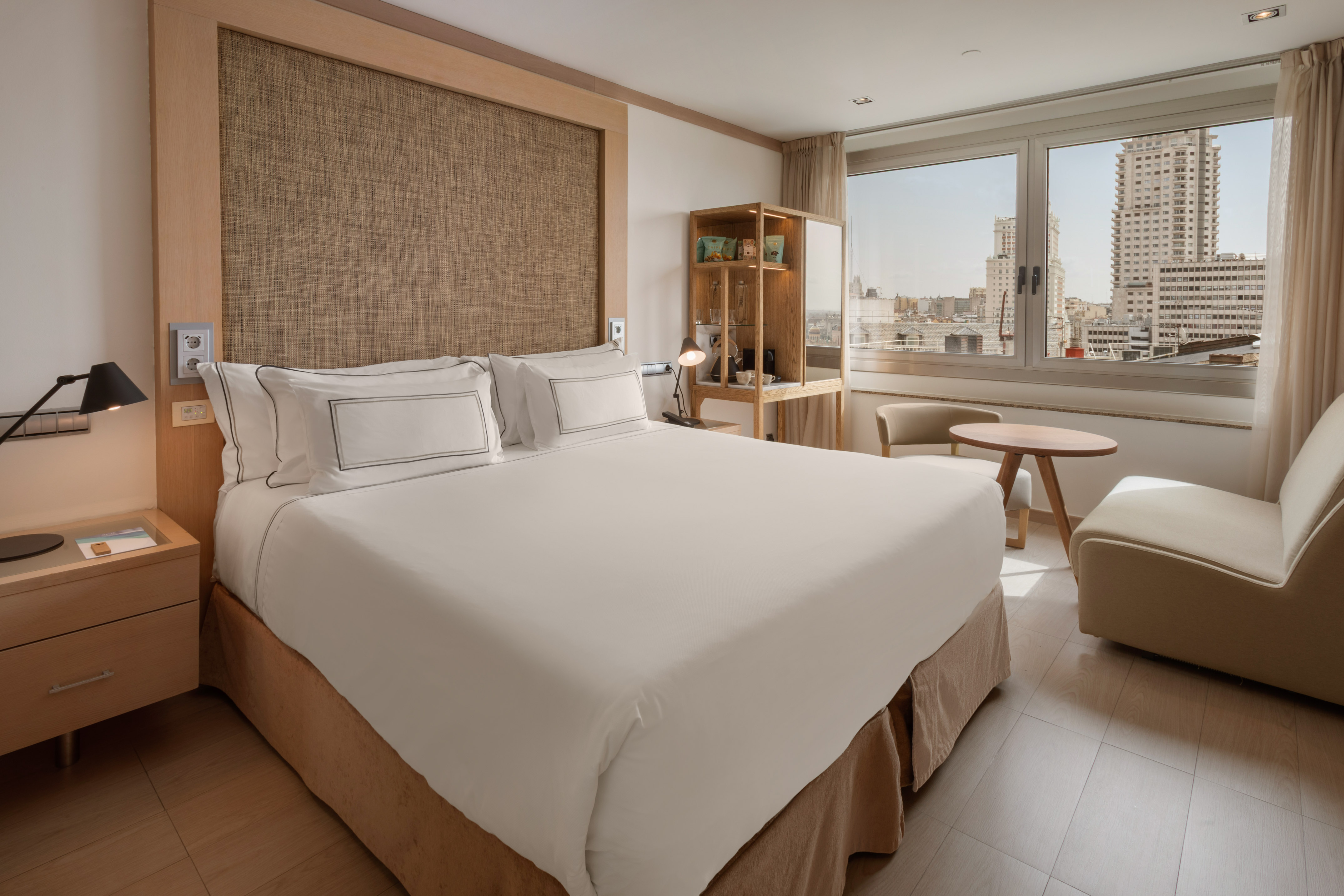 Hotel room with king bed, textured headboard, city view, and sitting area.