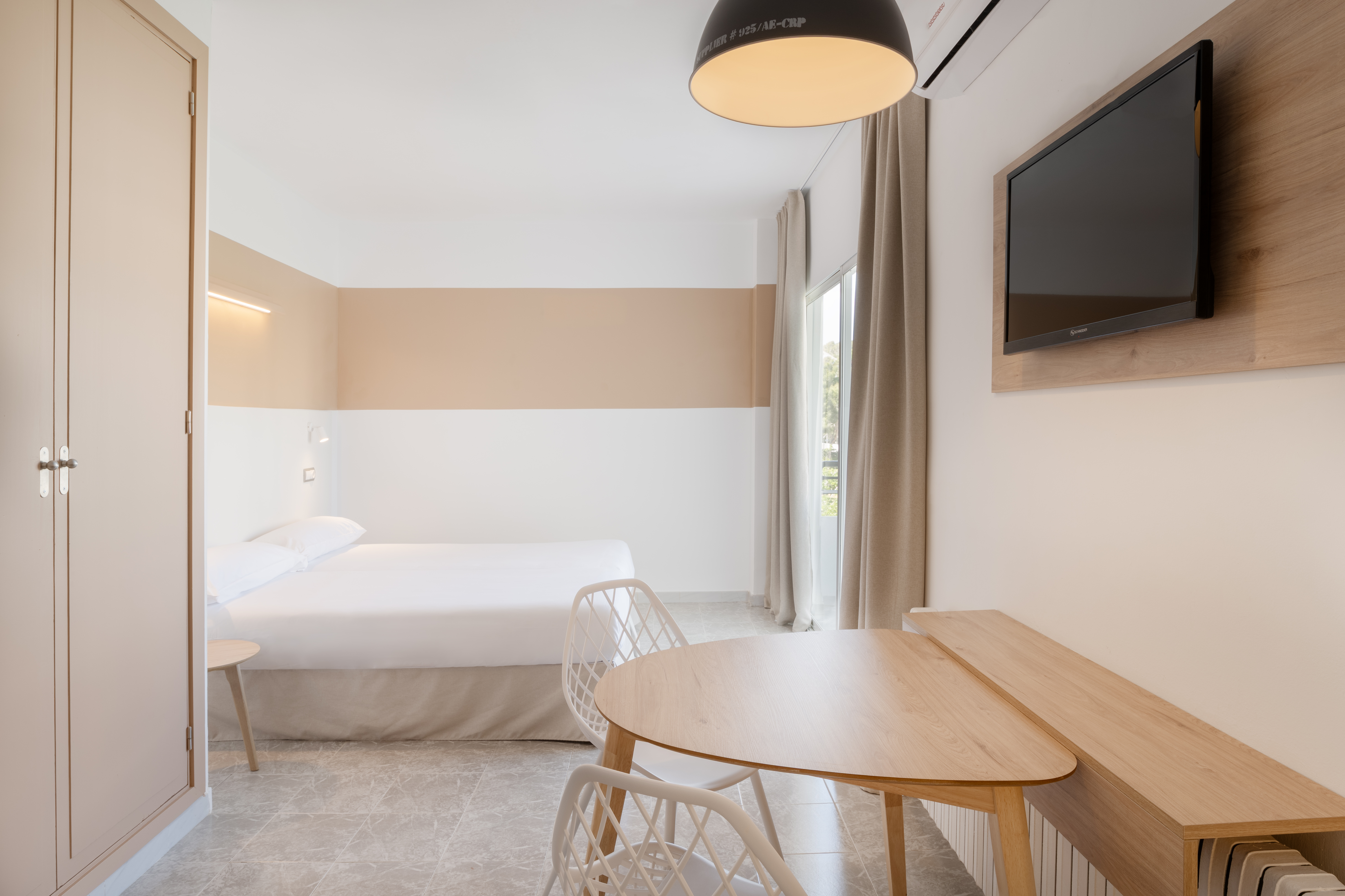Modern hotel studio with white bed, dining table, TV, and neutral decor.