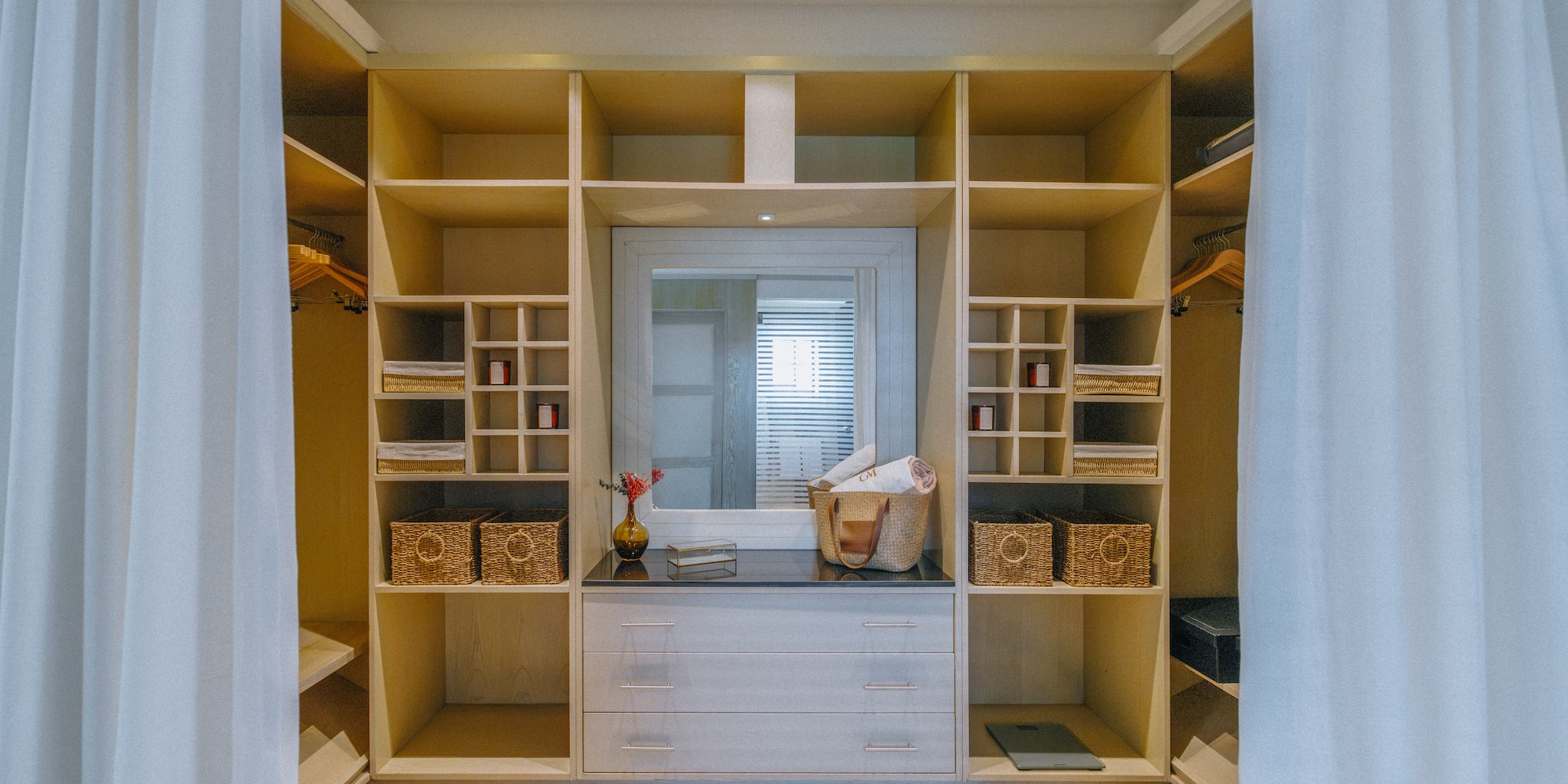 Organized walk-in closet with light wood shelving, central mirror, and dresser.