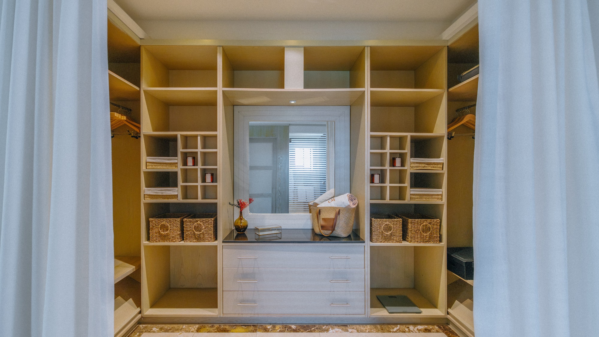 Organized walk-in closet with light wood shelving, central mirror, and dresser.