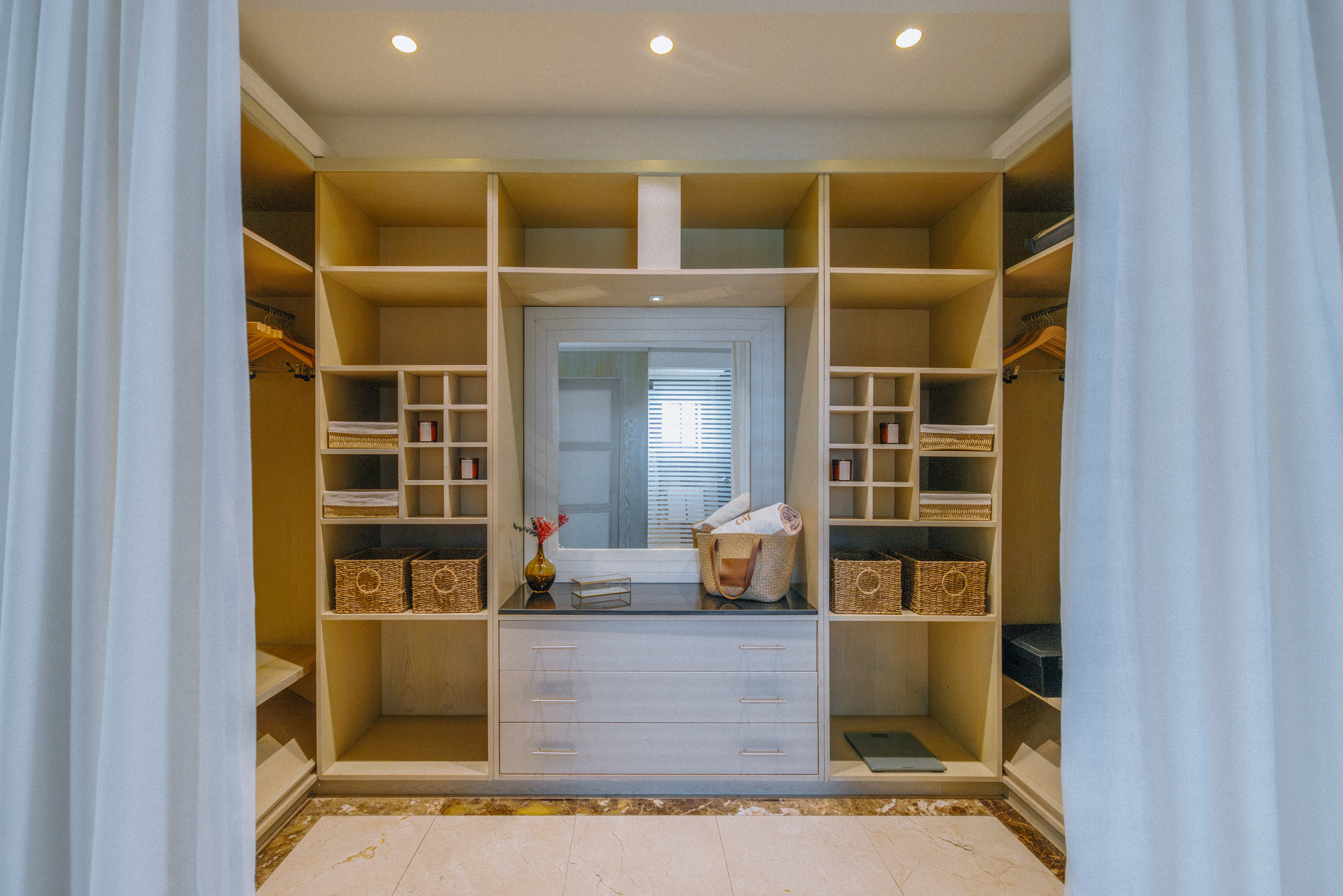 Organized walk-in closet with light wood shelving, central mirror, and dresser.