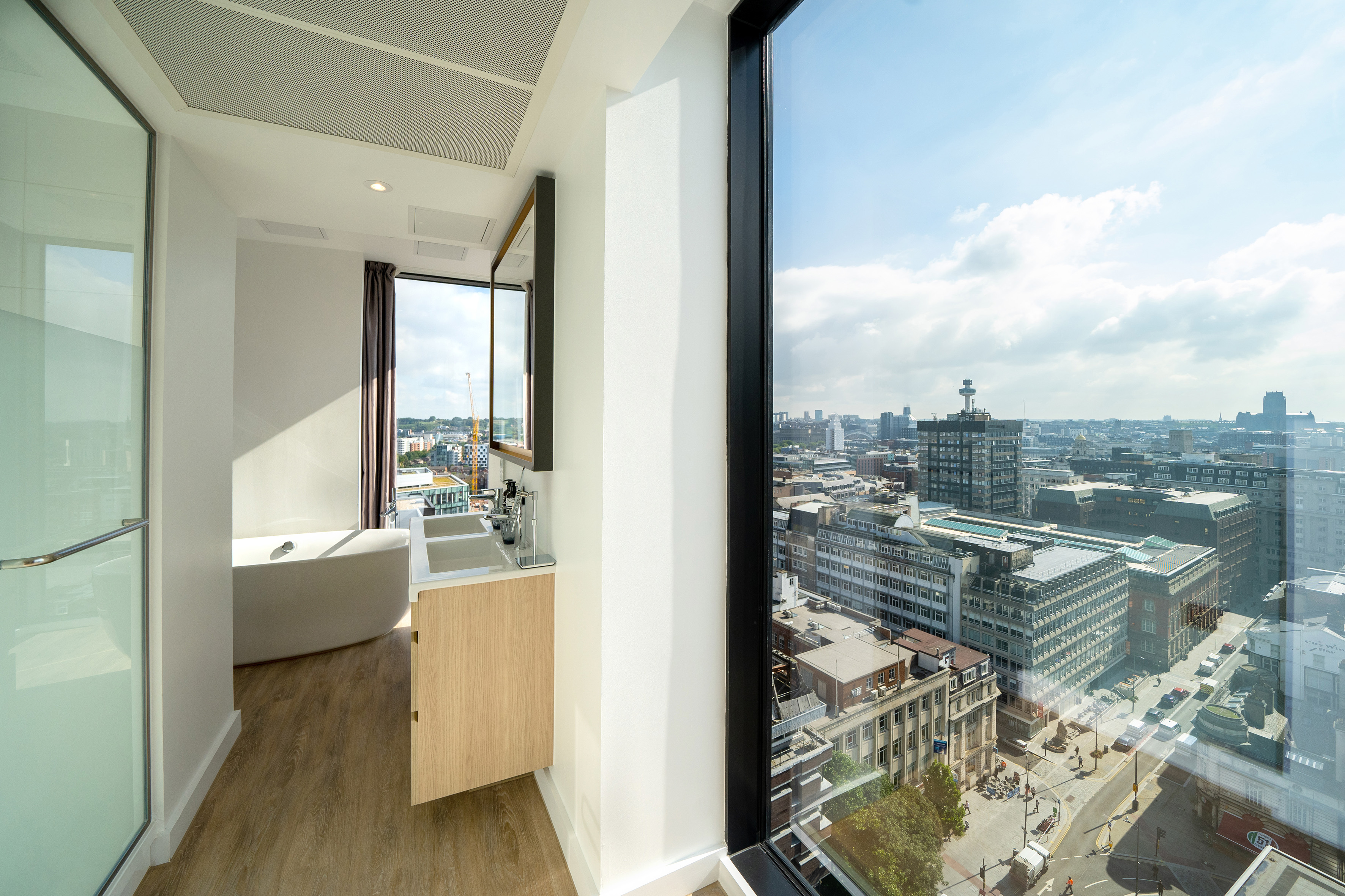 Modern bathroom with city skyline view, freestanding tub, and wood vanity.