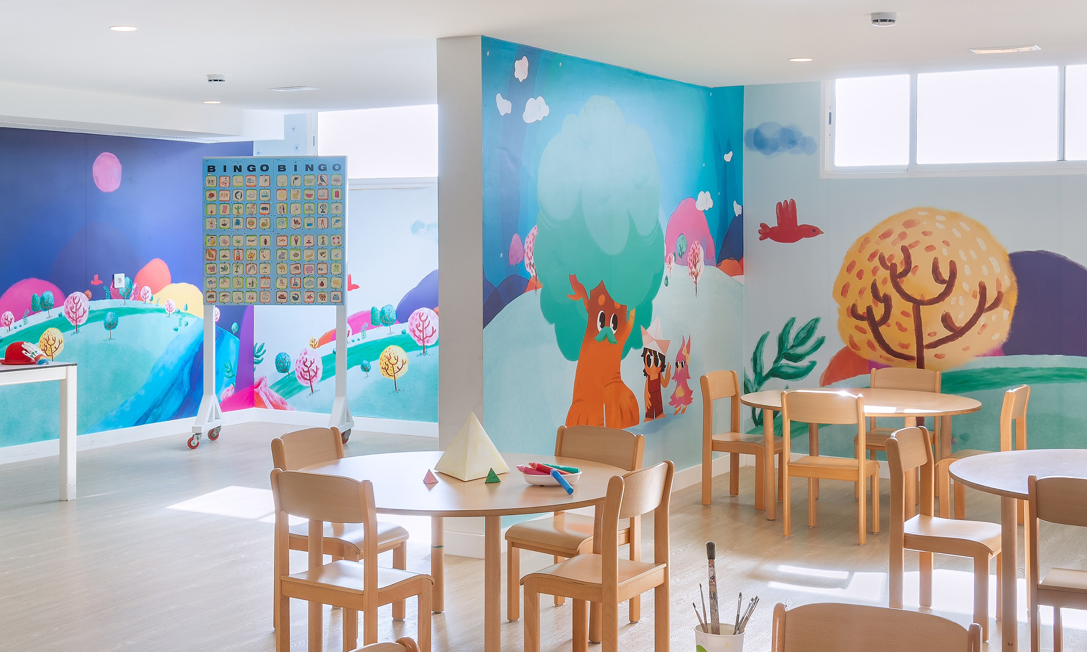 Colorful kids' activity room with cartoon murals, small tables, and chairs.