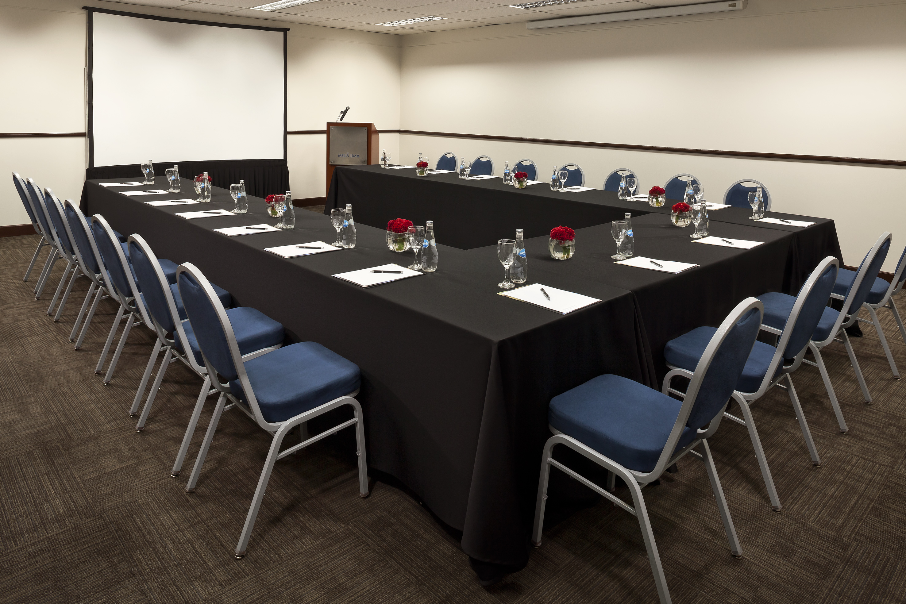 U-shaped conference room with blue chairs, black tables, and projector screen.