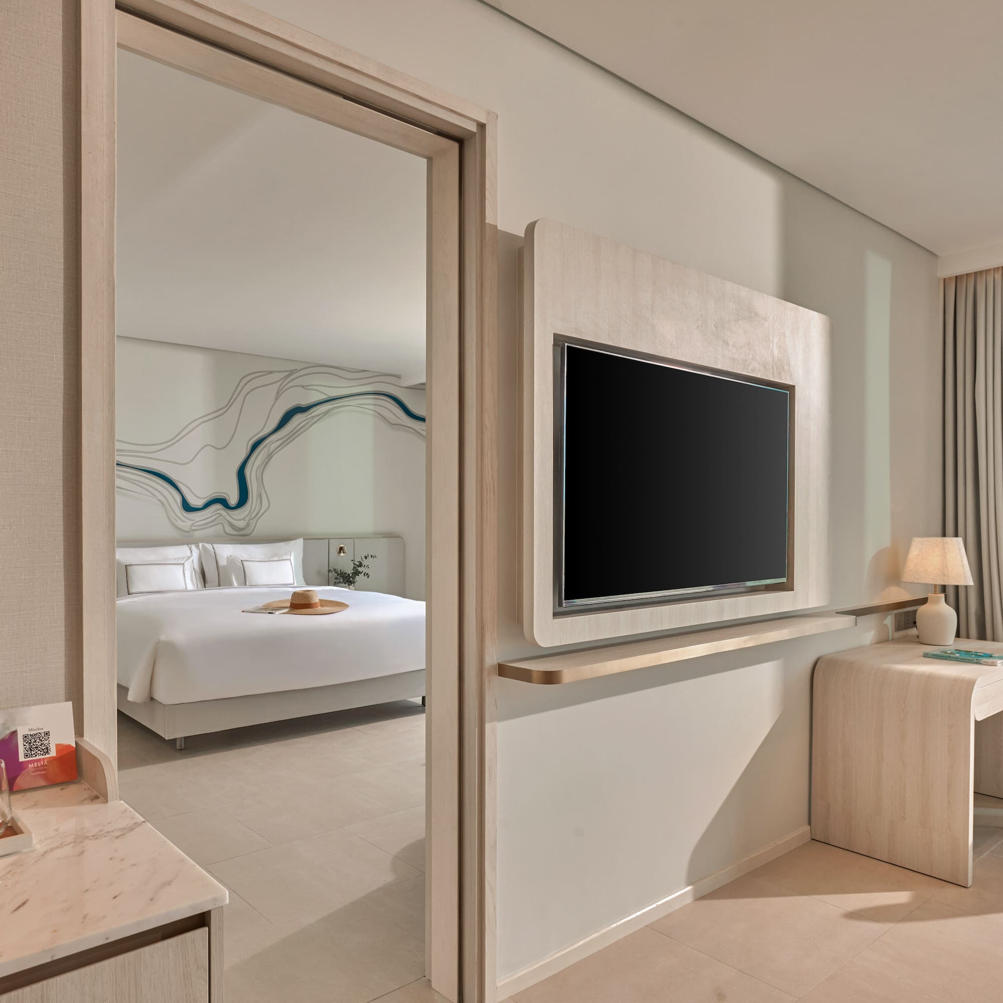 Modern hotel suite with open bedroom, TV, desk, and scenic mountain view.