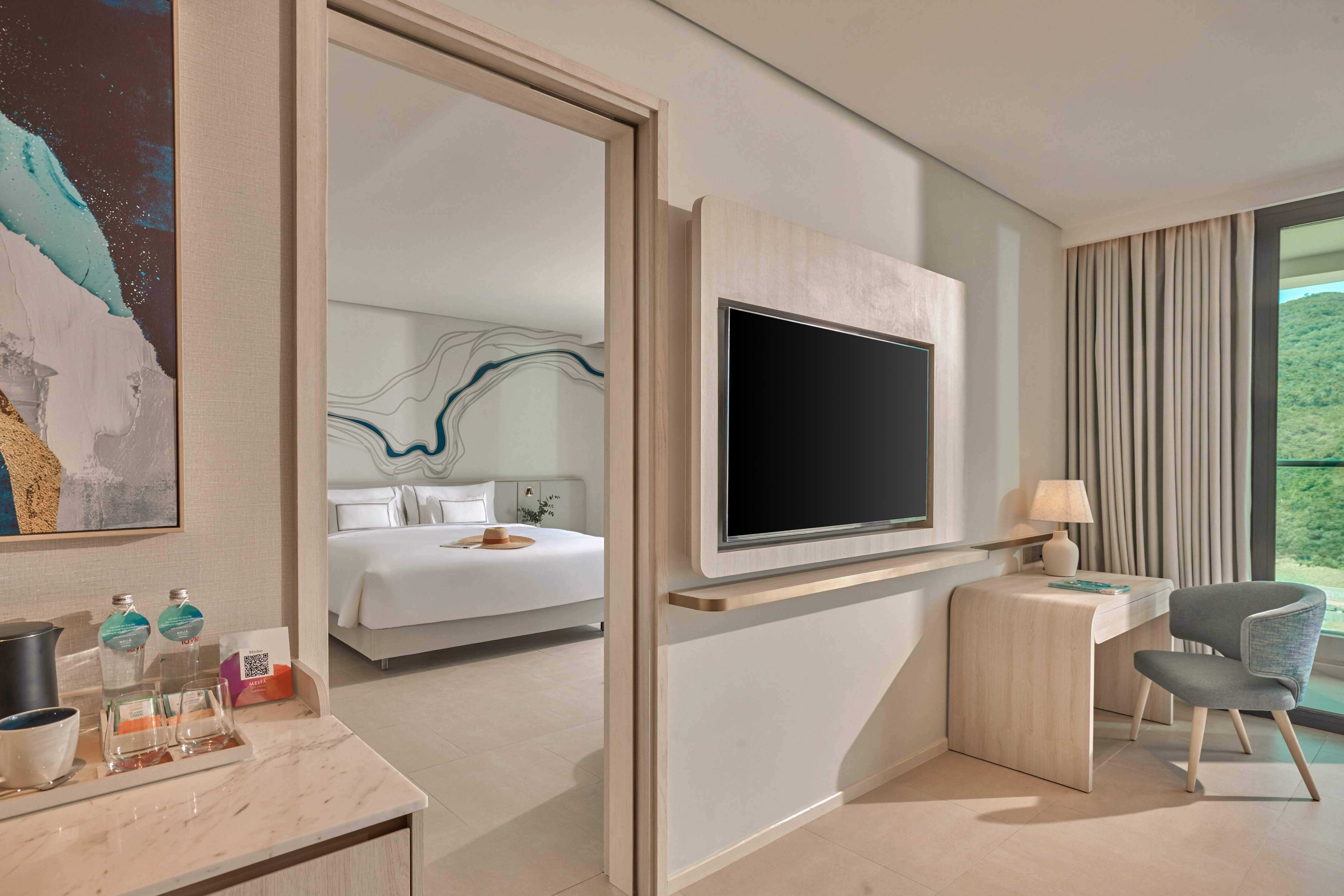 Modern hotel suite with open bedroom, TV, desk, and scenic mountain view.
