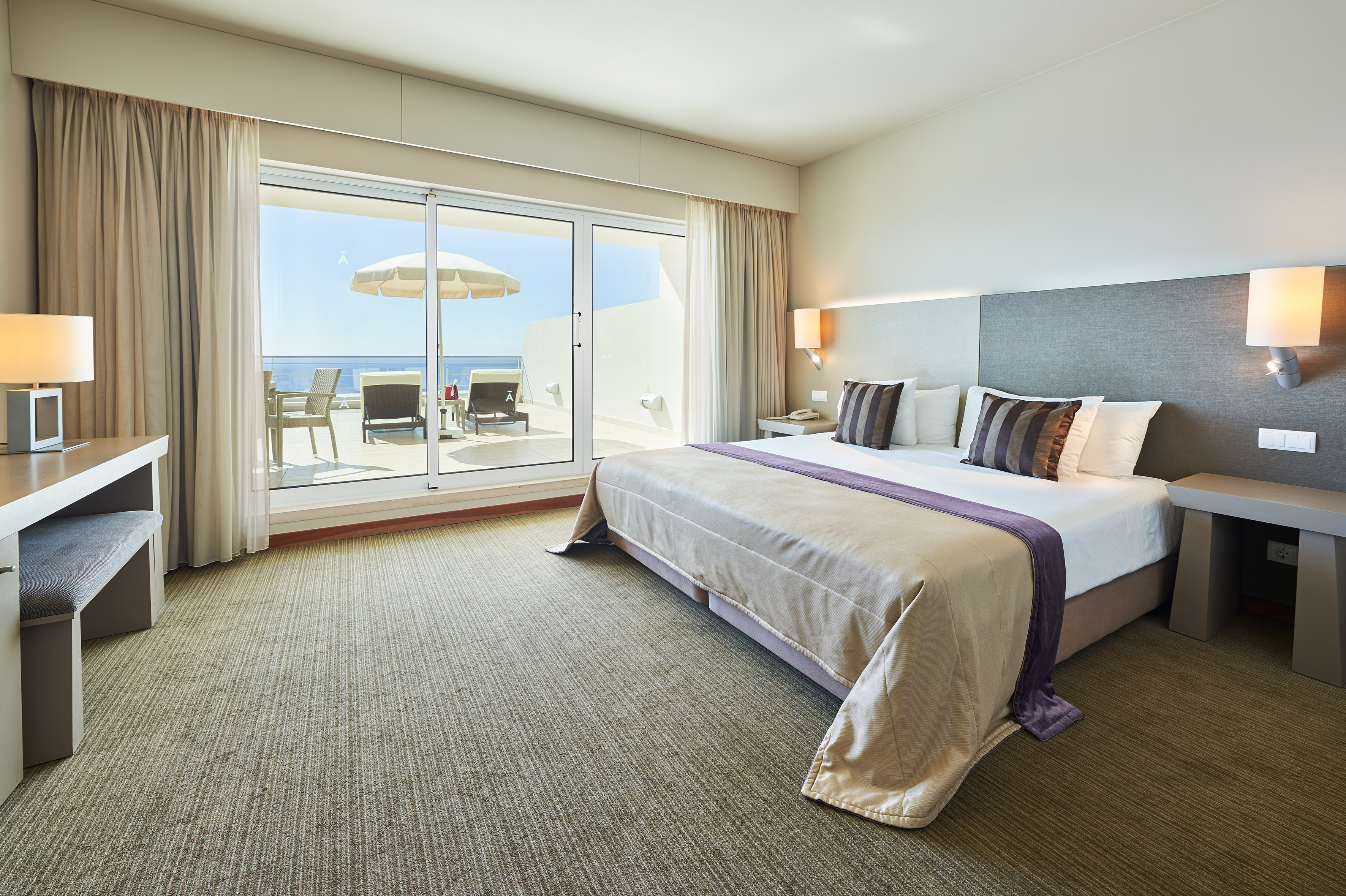Modern hotel bedroom with balcony, outdoor seating, and clear ocean view.