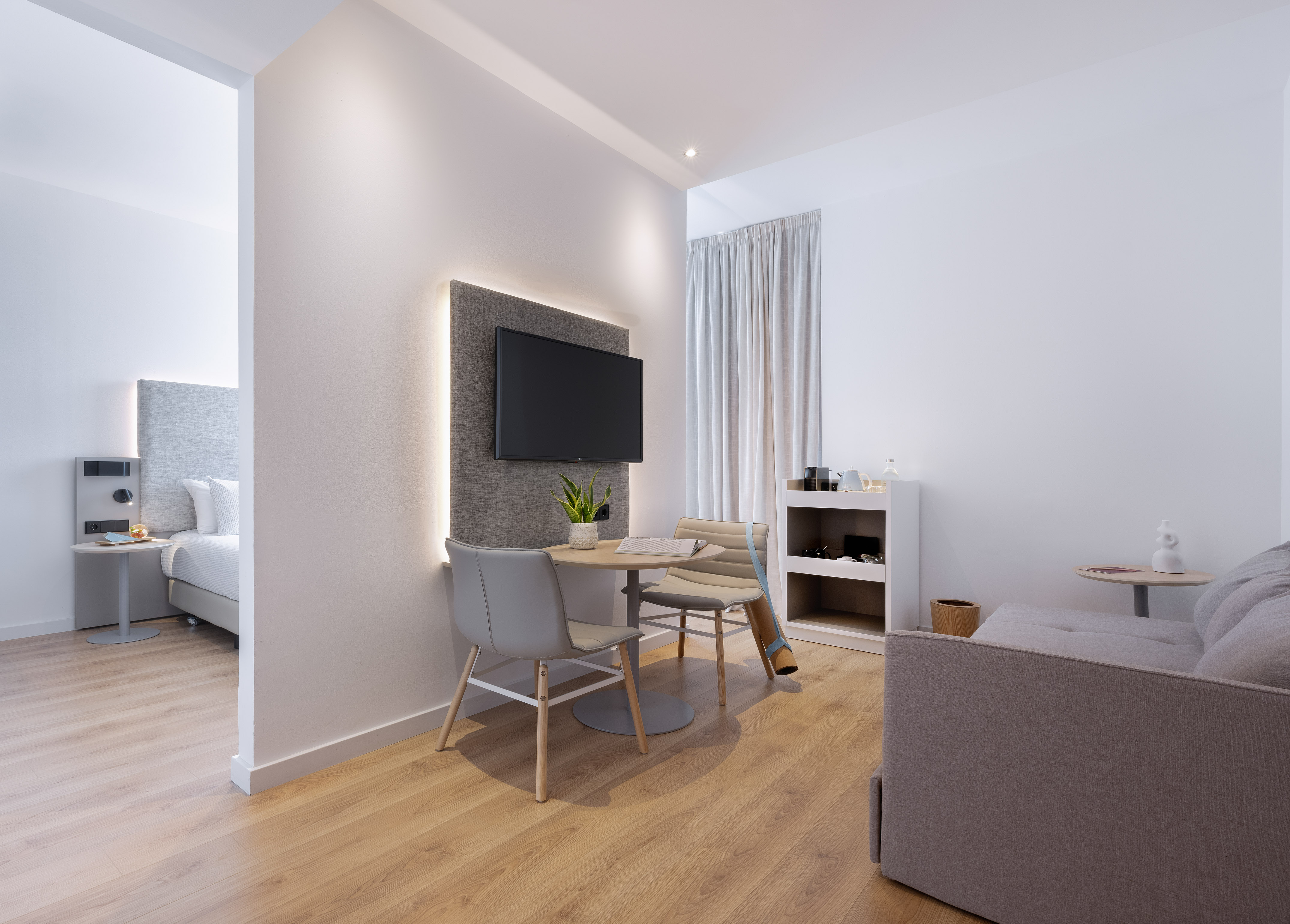 Modern hotel studio with living area, dining table, TV, and bedroom.