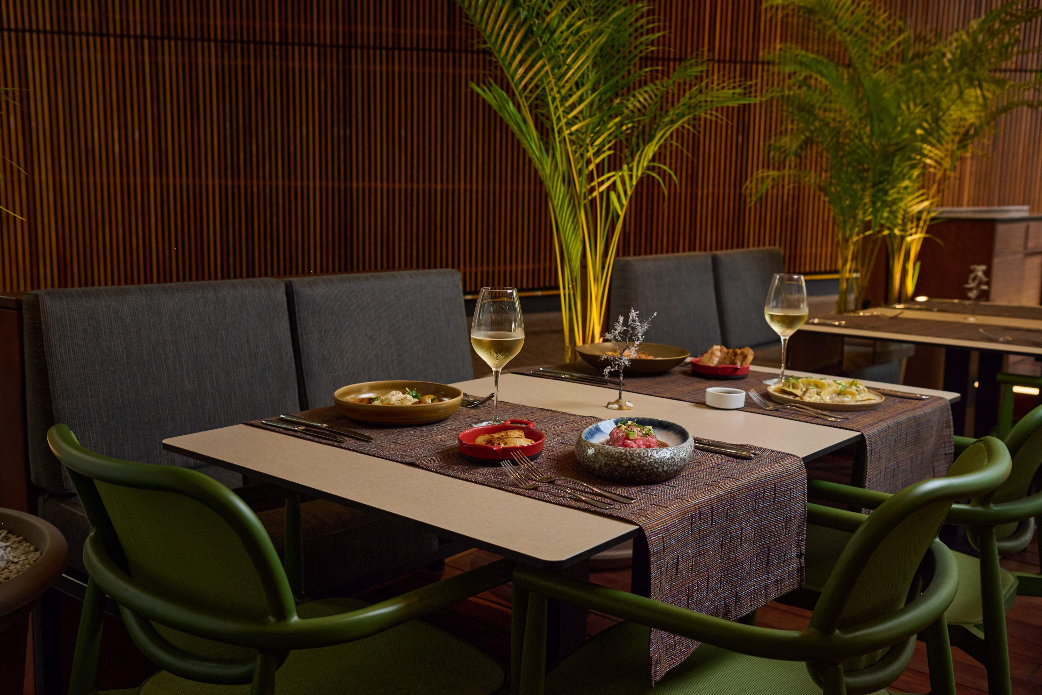 Fine dining table with appetizers, white wine, green chairs, and tropical plants.