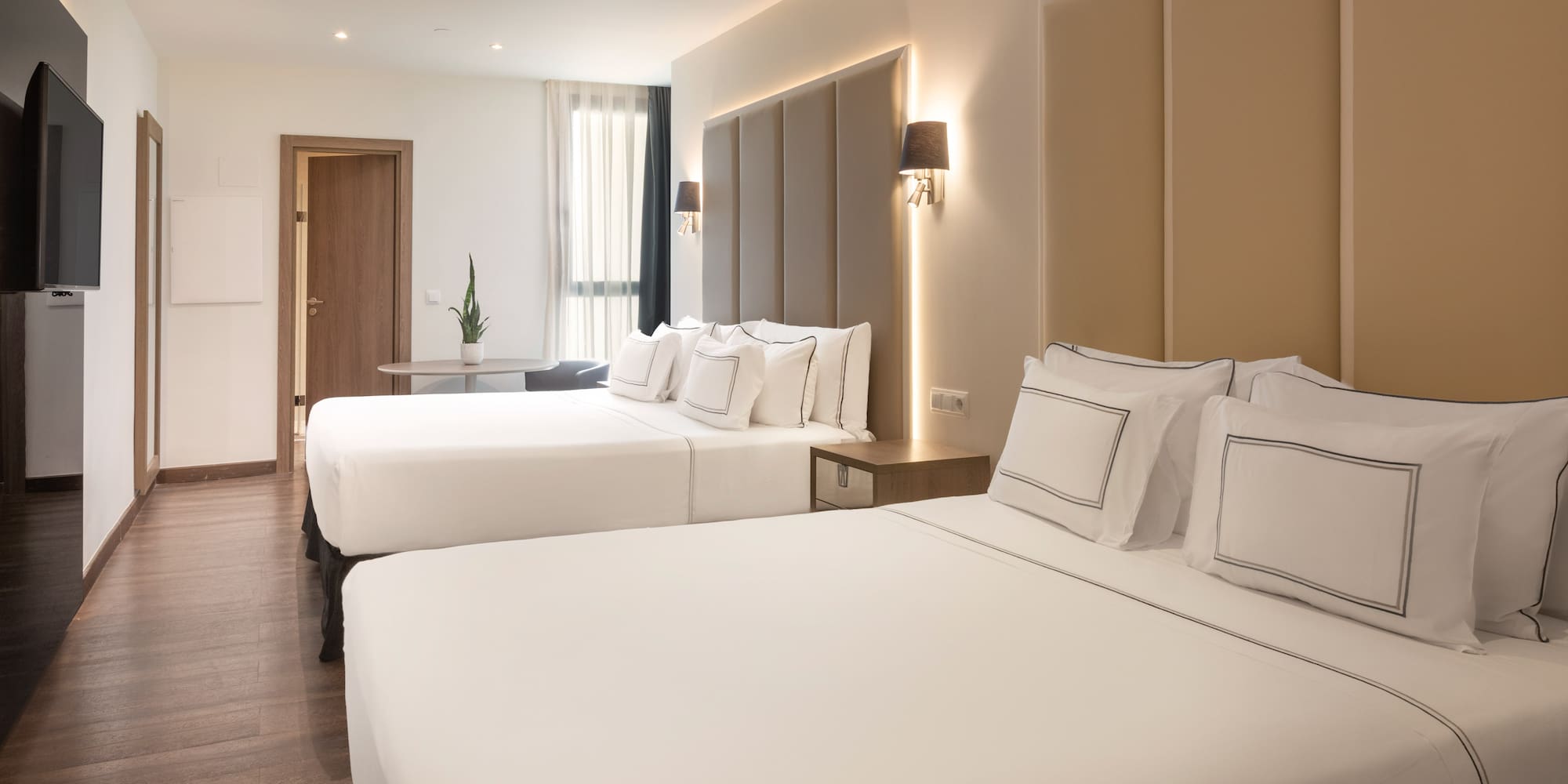Modern hotel room with two beds, hardwood floor, TV, and ambient lighting.