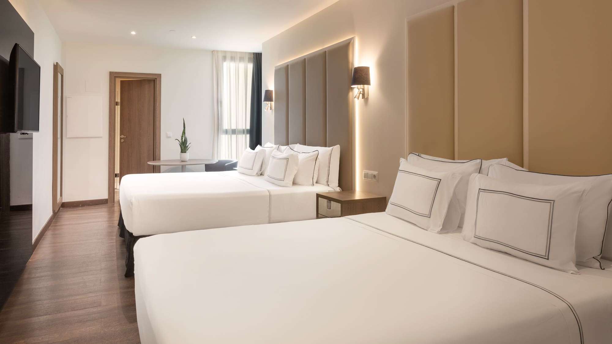 Modern hotel room with two beds, hardwood floor, TV, and ambient lighting.