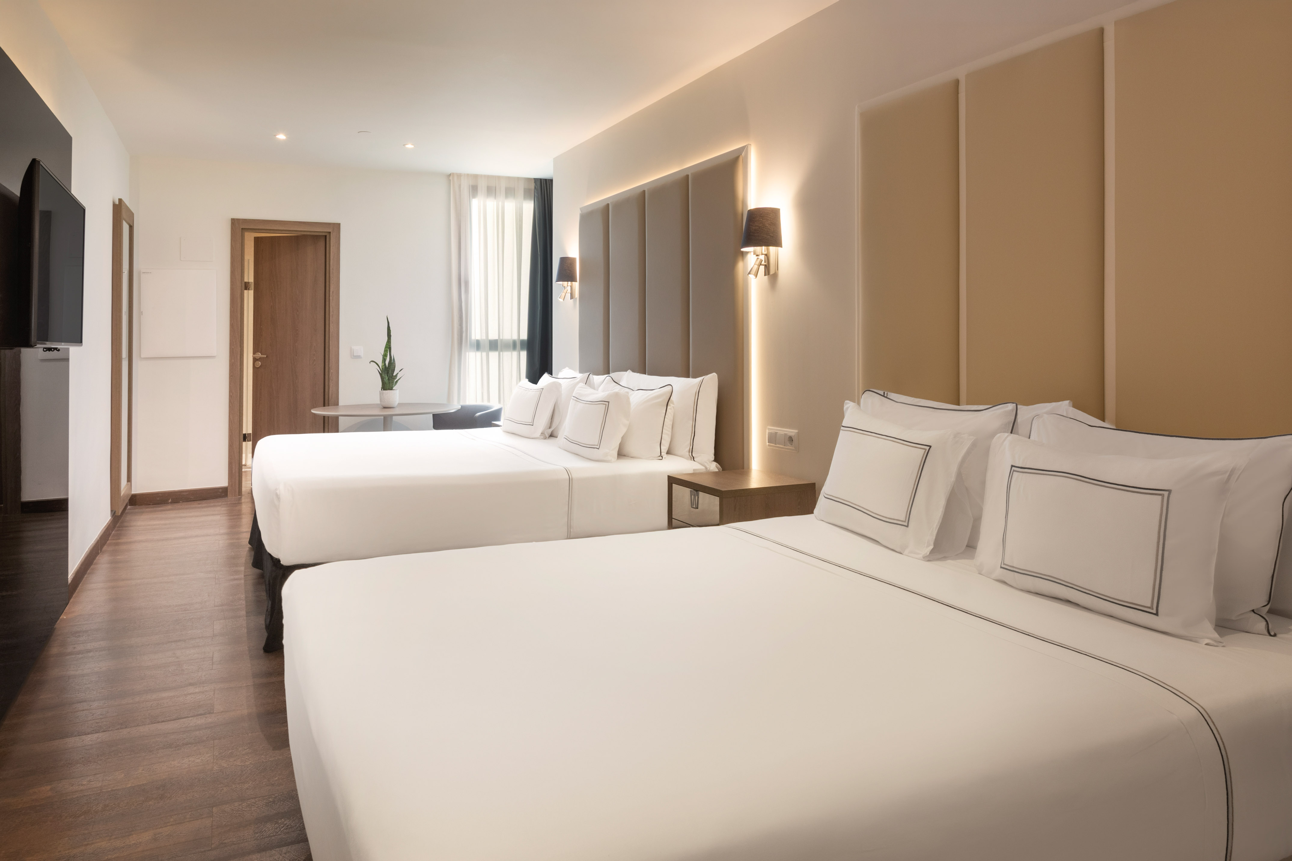 Modern hotel room with two beds, hardwood floor, TV, and ambient lighting.