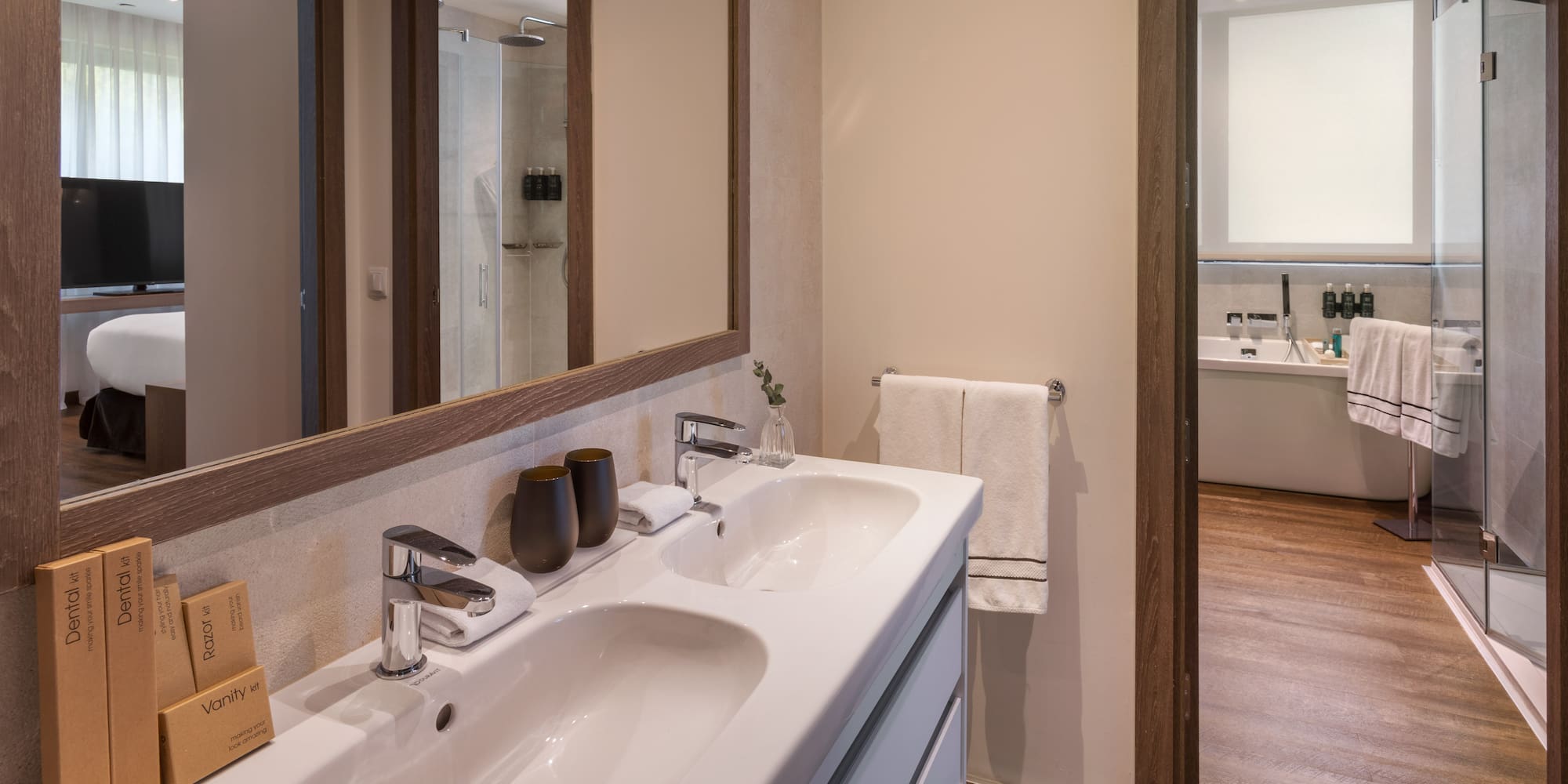 Baño moderno hotel: lavabo doble, espejo, ducha y artículos de tocador.