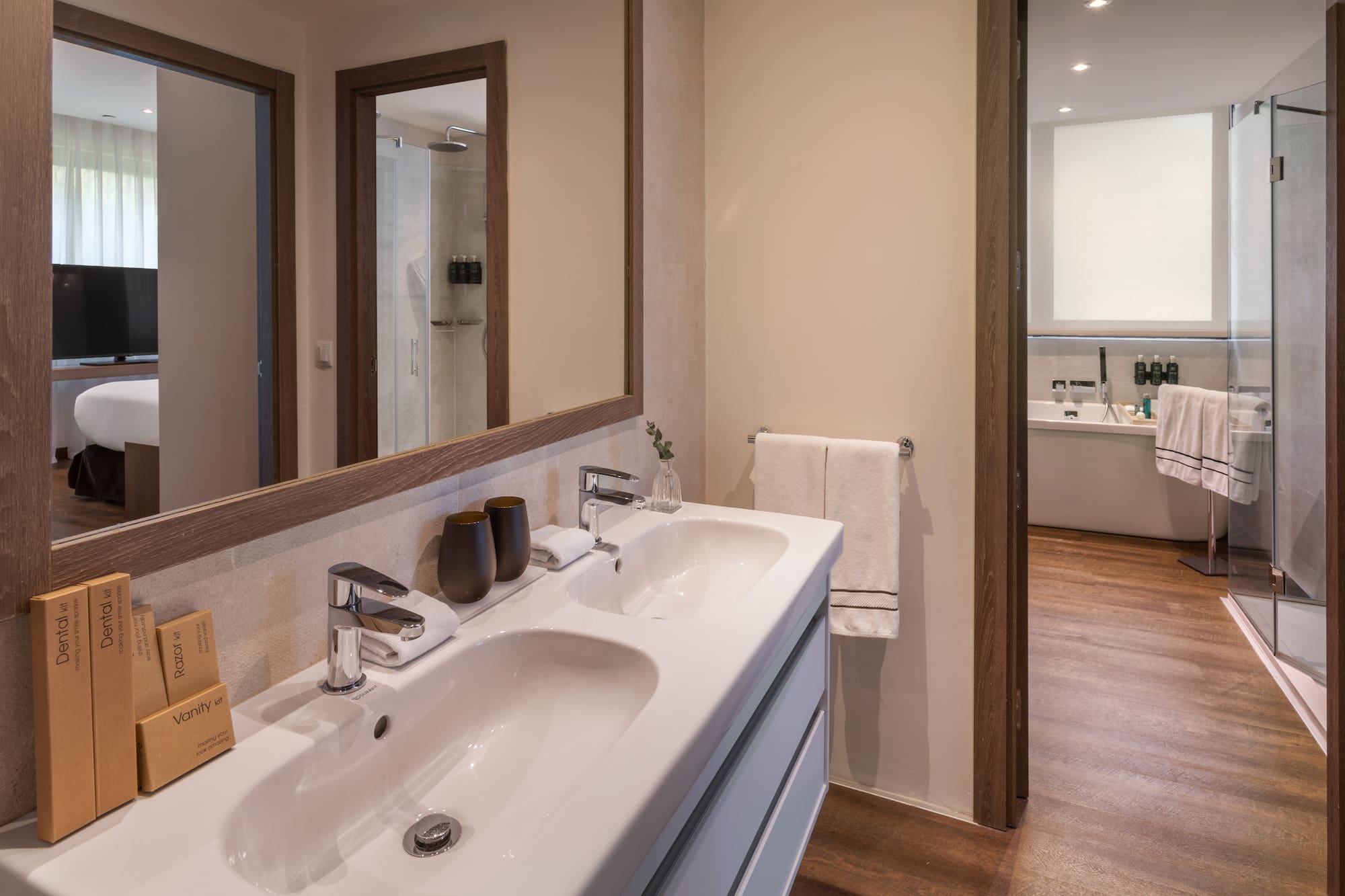 Baño moderno hotel: lavabo doble, espejo, ducha y artículos de tocador.