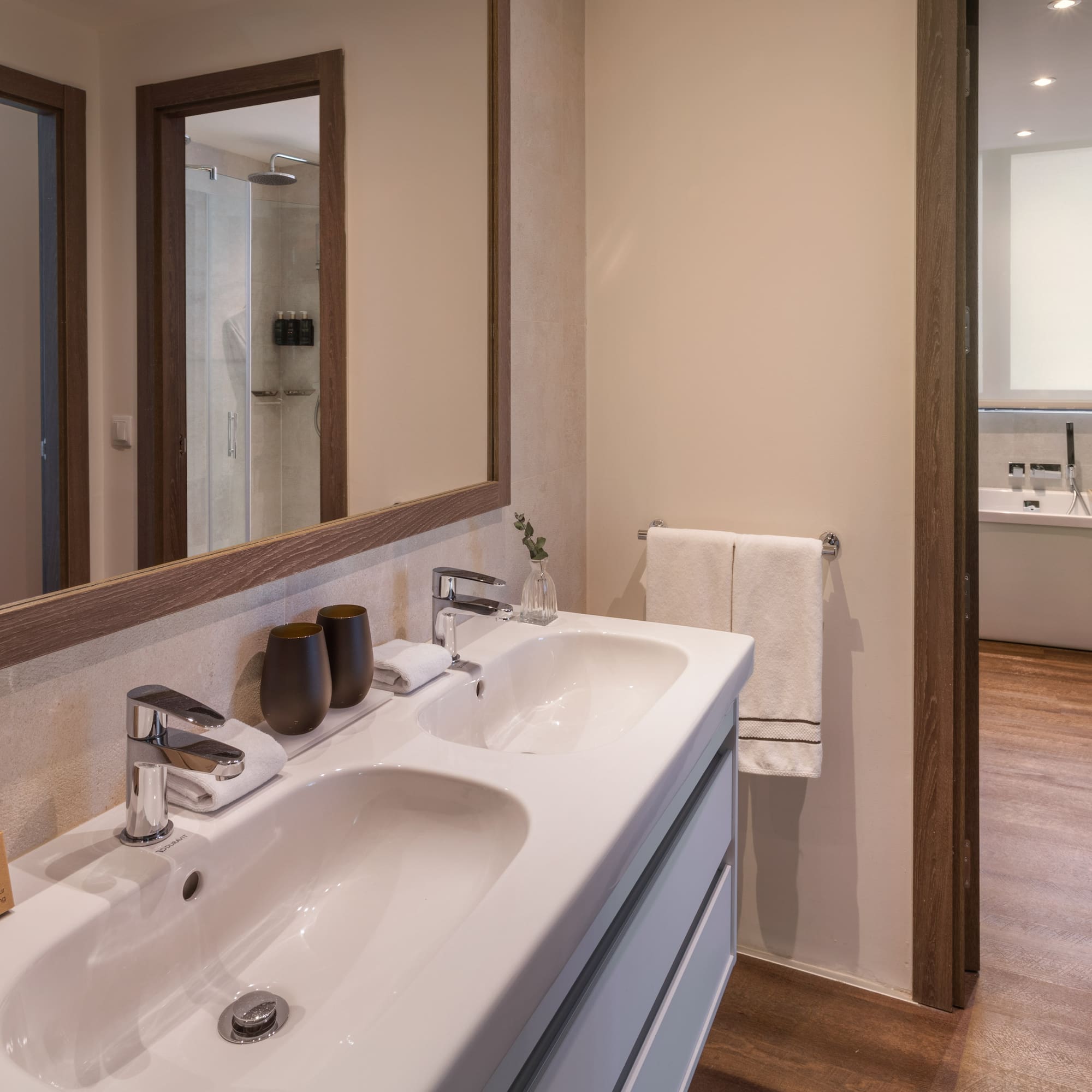 Baño moderno hotel: lavabo doble, espejo, ducha y artículos de tocador.