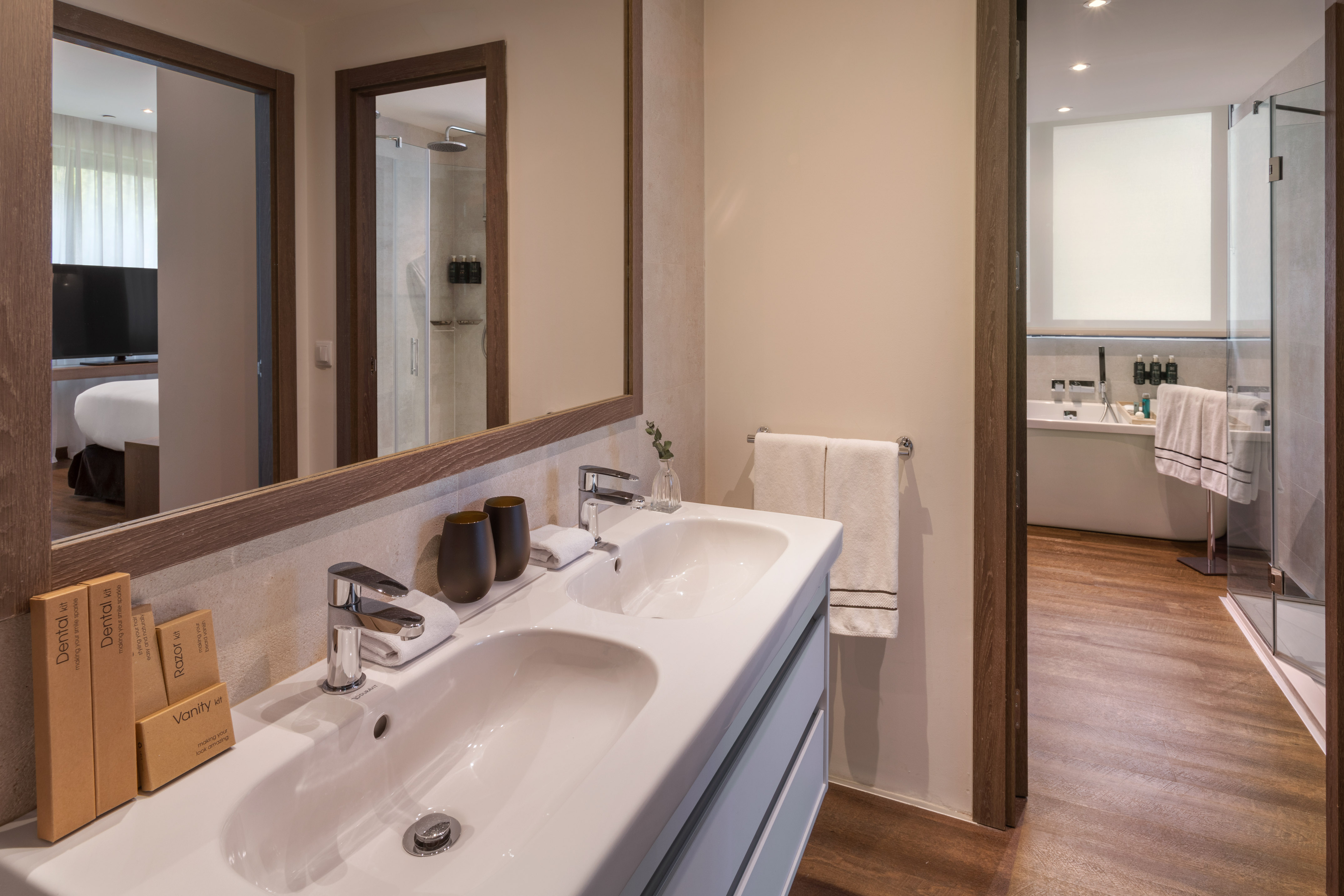 Baño moderno hotel: lavabo doble, espejo, ducha y artículos de tocador.