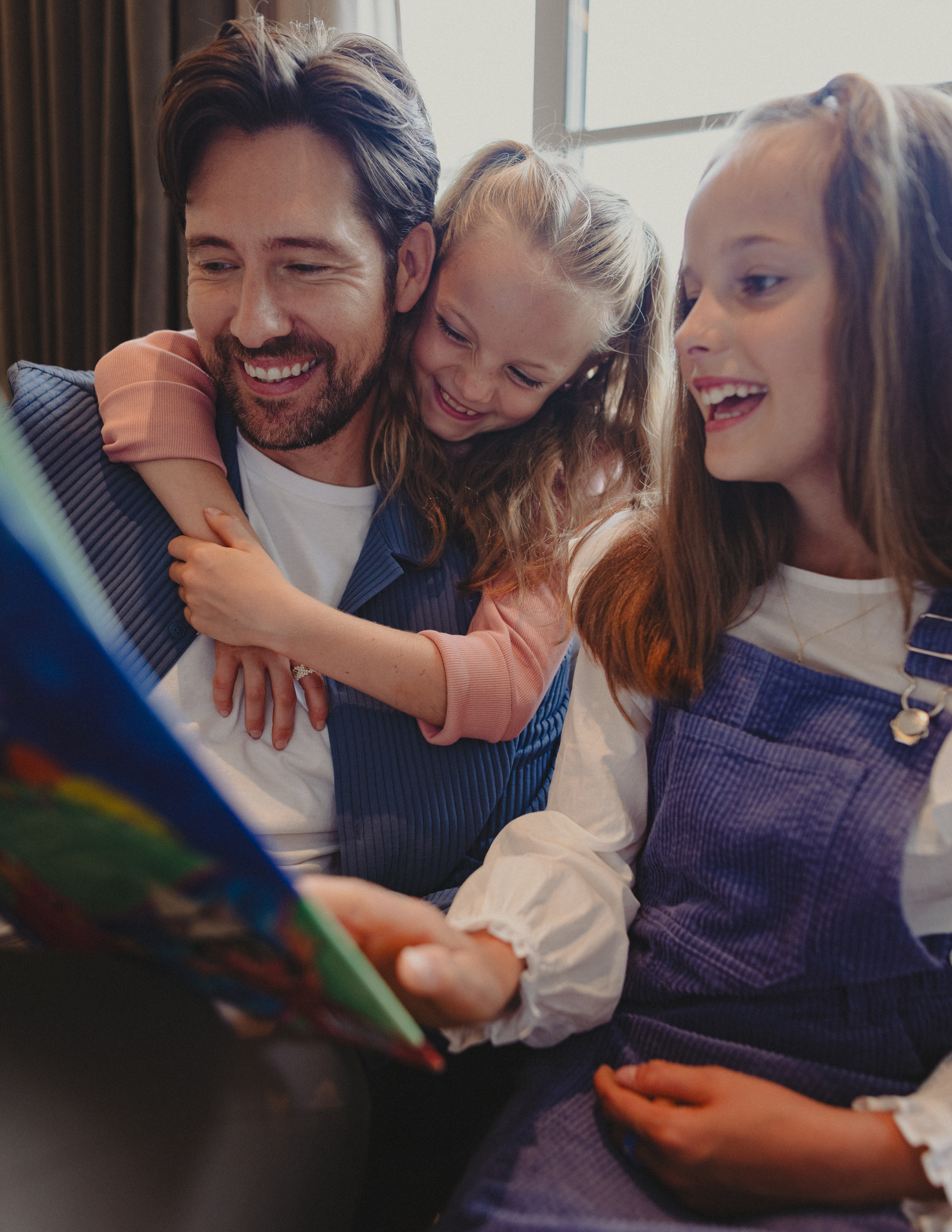 Happy father reading a book to his two smiling daughters, family bonding time.