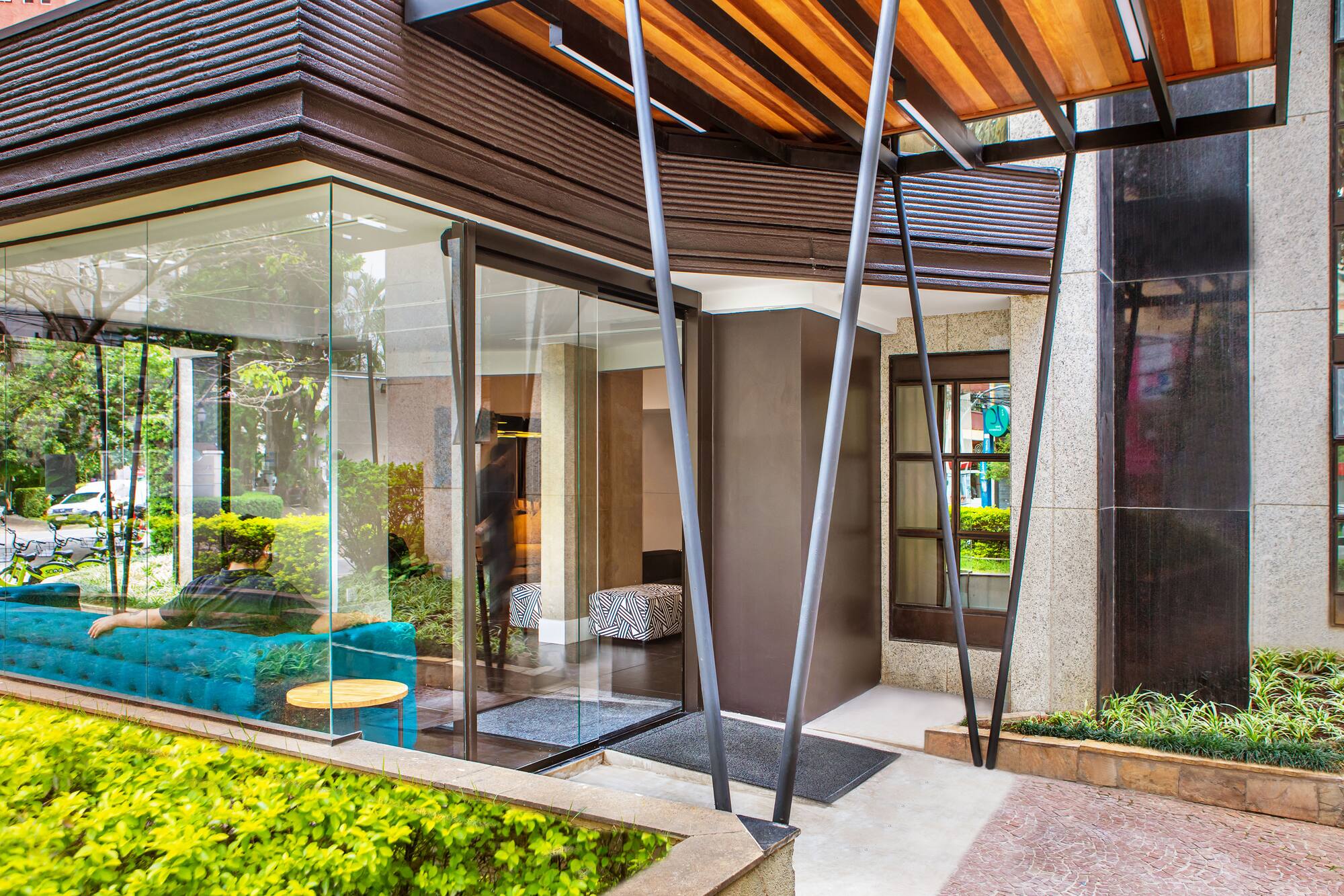 Modern building entrance with glass facade, wood canopy, and teal sofa.