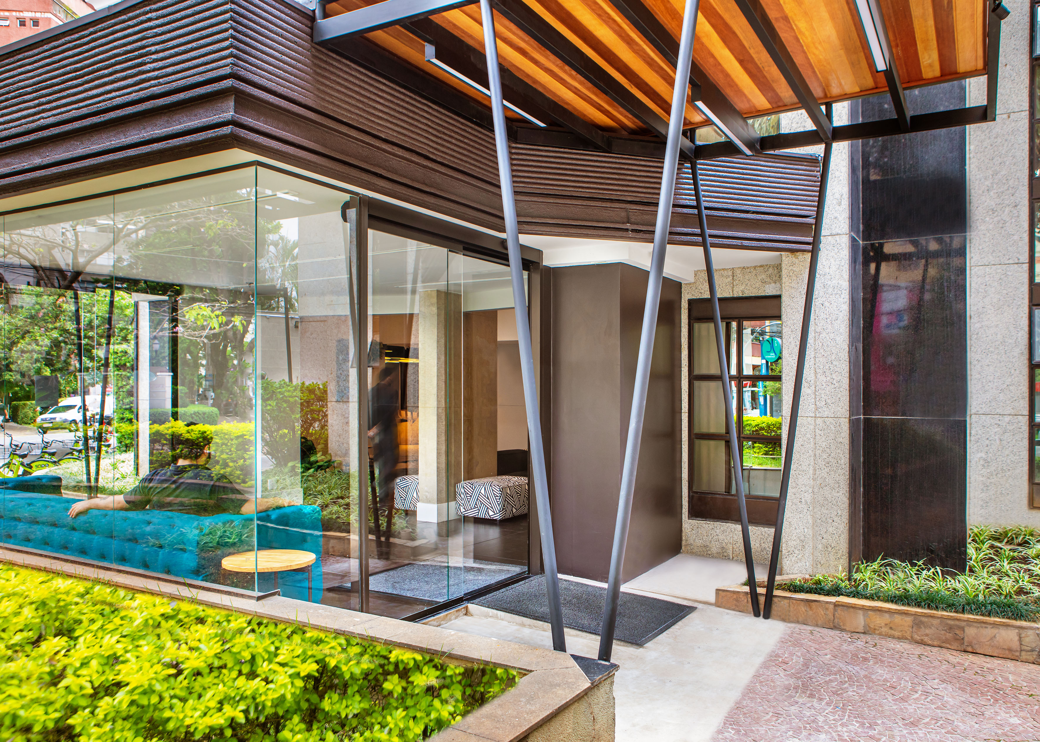 Modern building entrance with glass facade, wood canopy, and teal sofa.