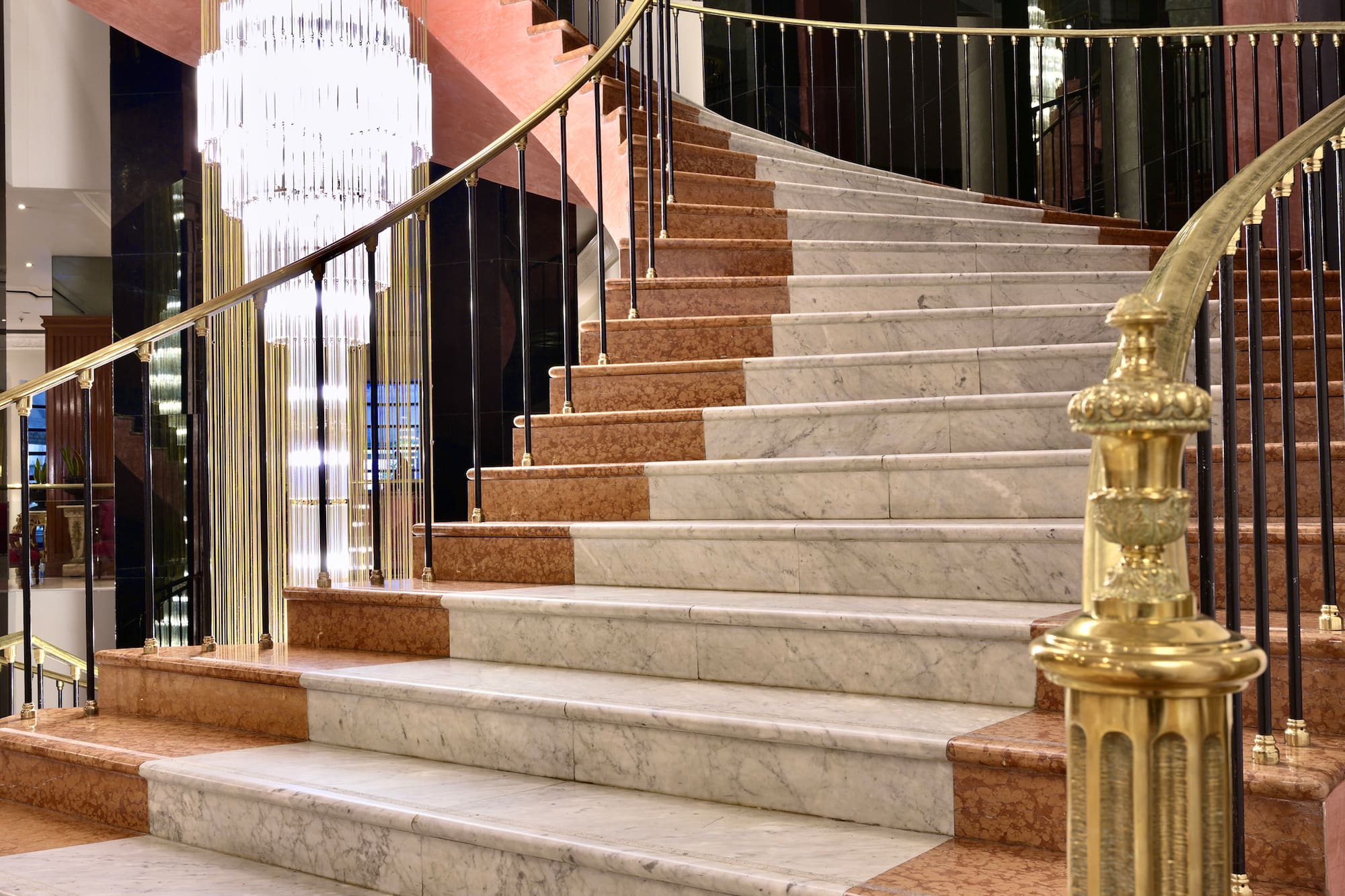 Grand marble spiral staircase with golden railing and crystal chandelier.