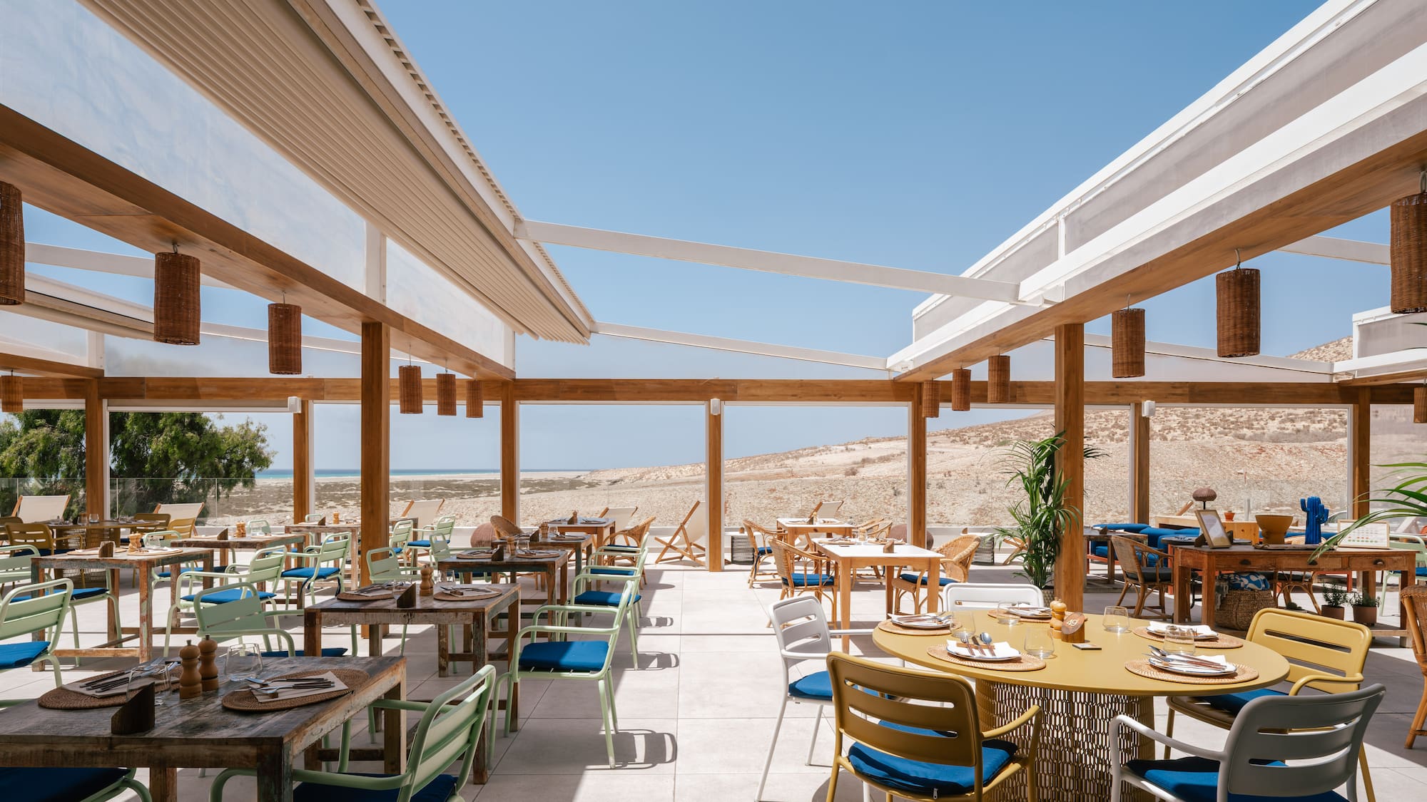 Outdoor restaurant patio with modern tables, desert beach view, under clear sky.