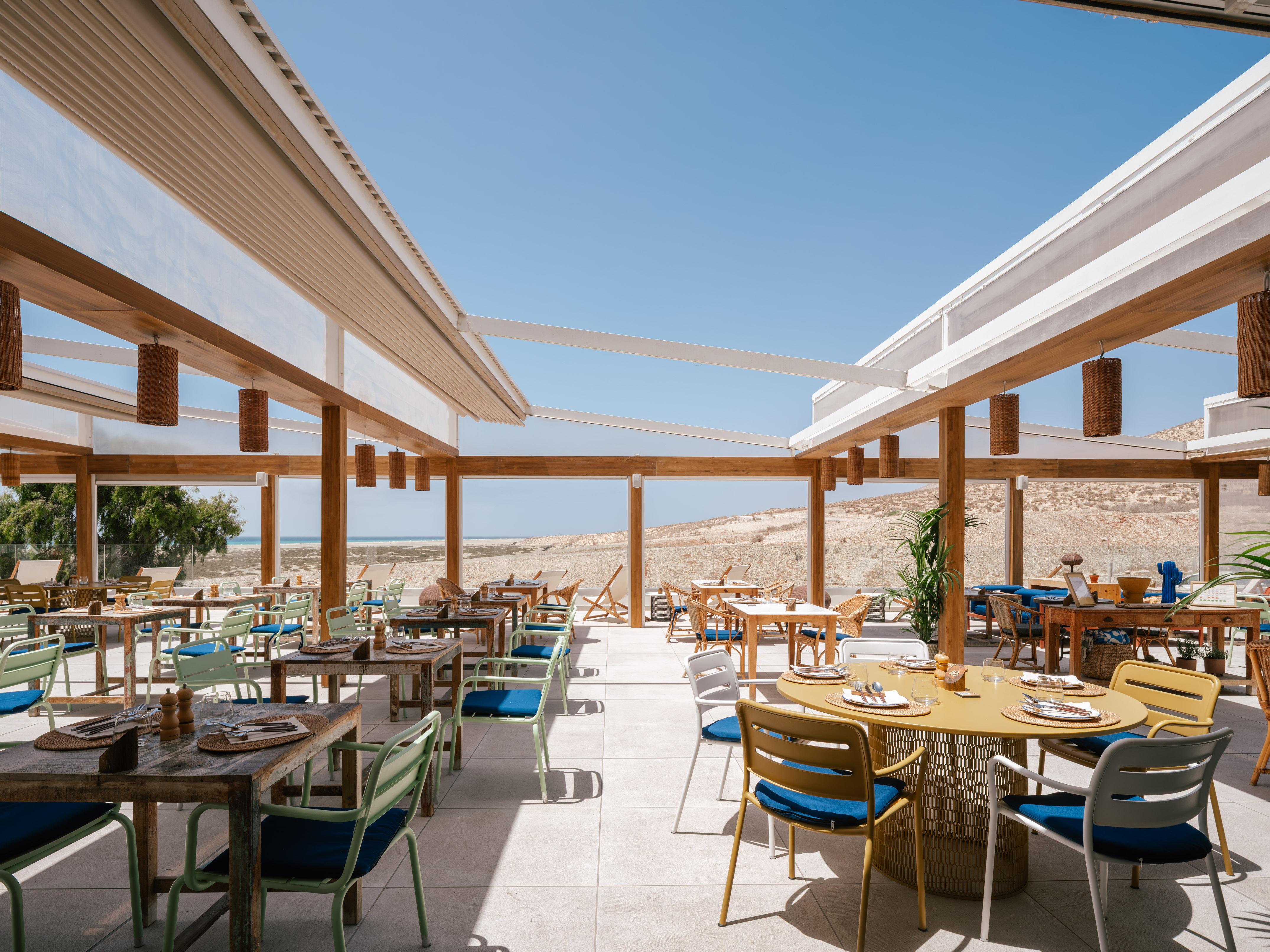 Outdoor restaurant patio with modern tables, desert beach view, under clear sky.