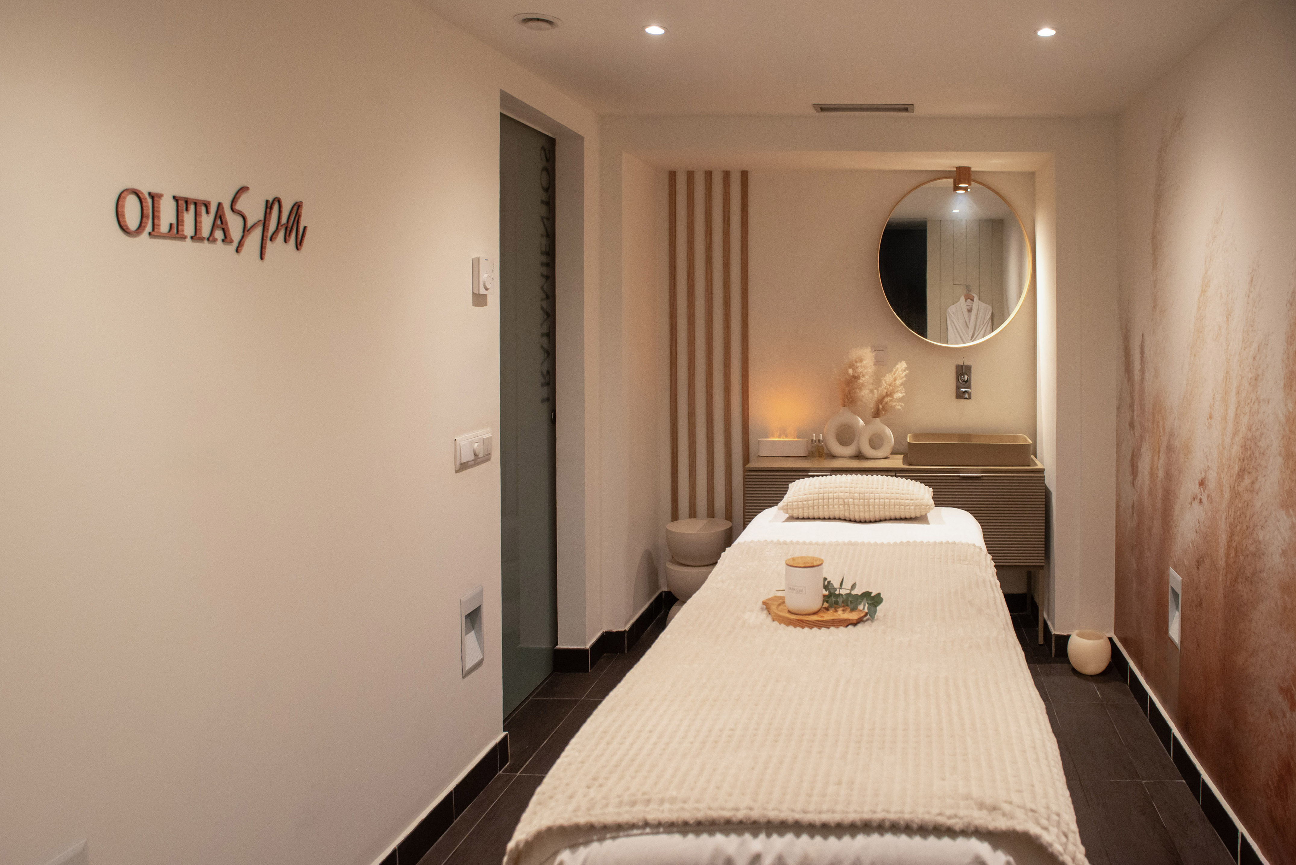 Olita Spa treatment room with massage bed, round mirror, and soothing decor.