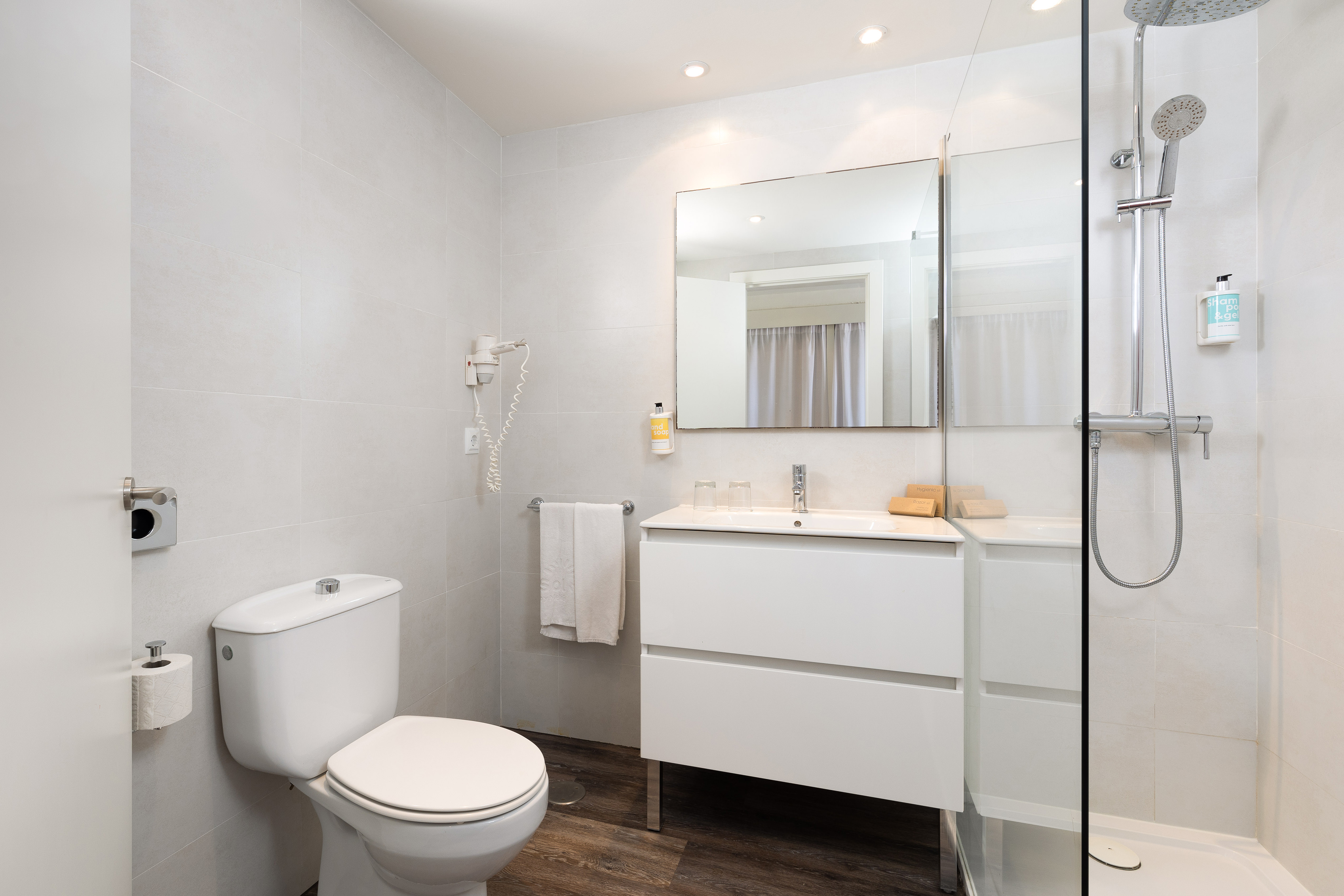 Contemporary hotel bathroom with white tiles, shower, vanity, and toilet.