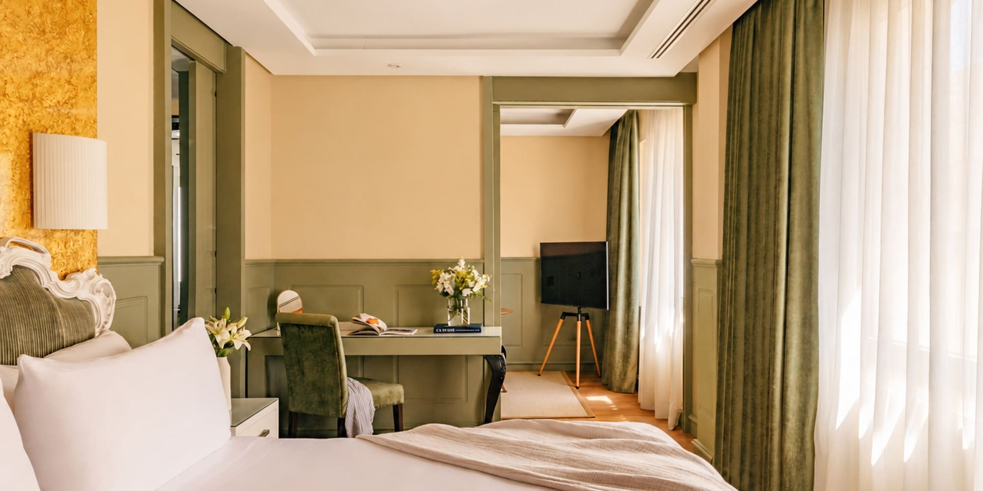 Elegant hotel room with large bed, writing desk, TV, and green trim.
